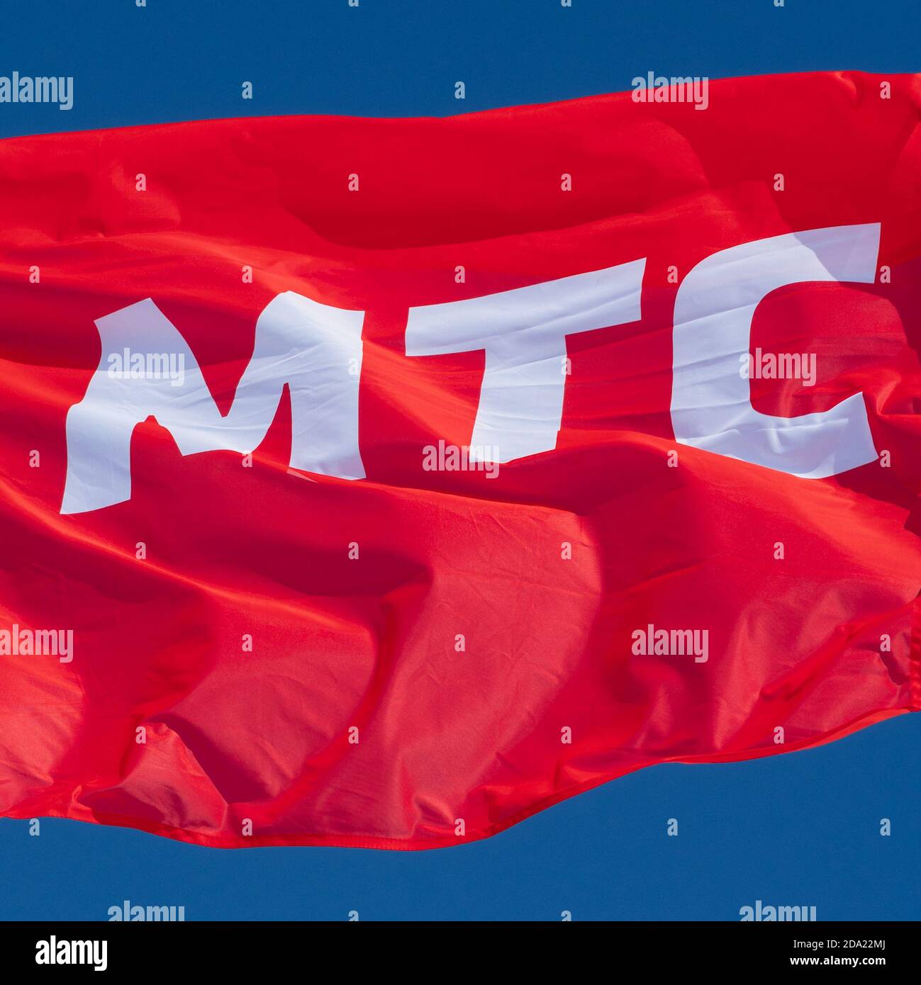 Red flag waving in wind with text in Russian: MTS Mobile TeleSystems, abbreviation mobile operator Russian Federation. Brand flag on background sky Stock Photo