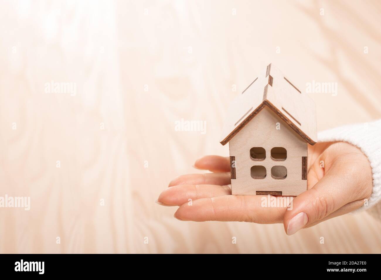 Woman hand holding small wooden toy house on natural wooden blur ...