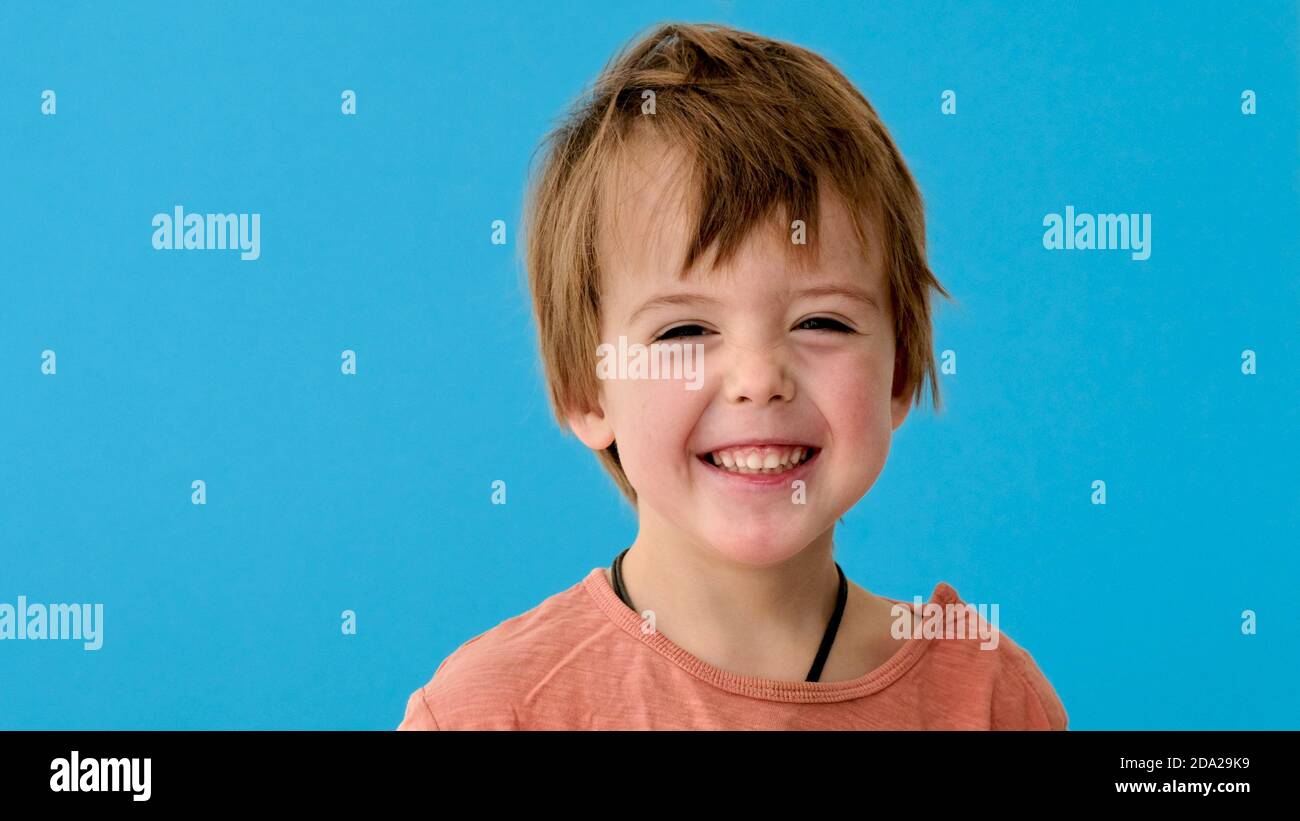 Little boy in orange tshirt smiles on turquoise background Stock Photo
