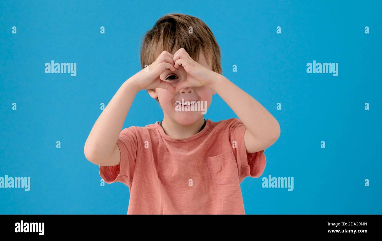 Kid makes heart with fingers posing for camera on turquoise Stock Photo