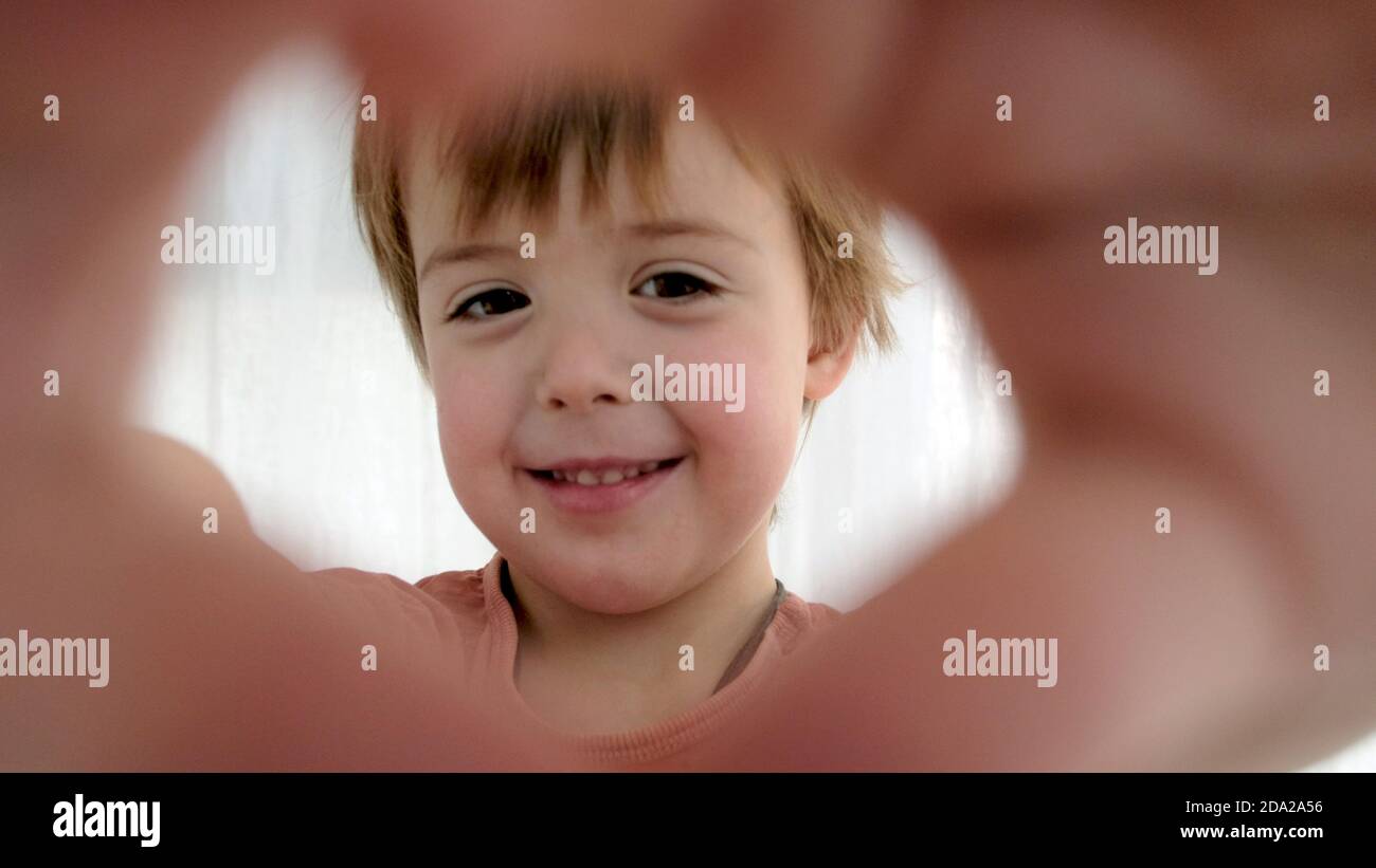 Playful kid makes heart with fingers as frame on camera Stock Photo
