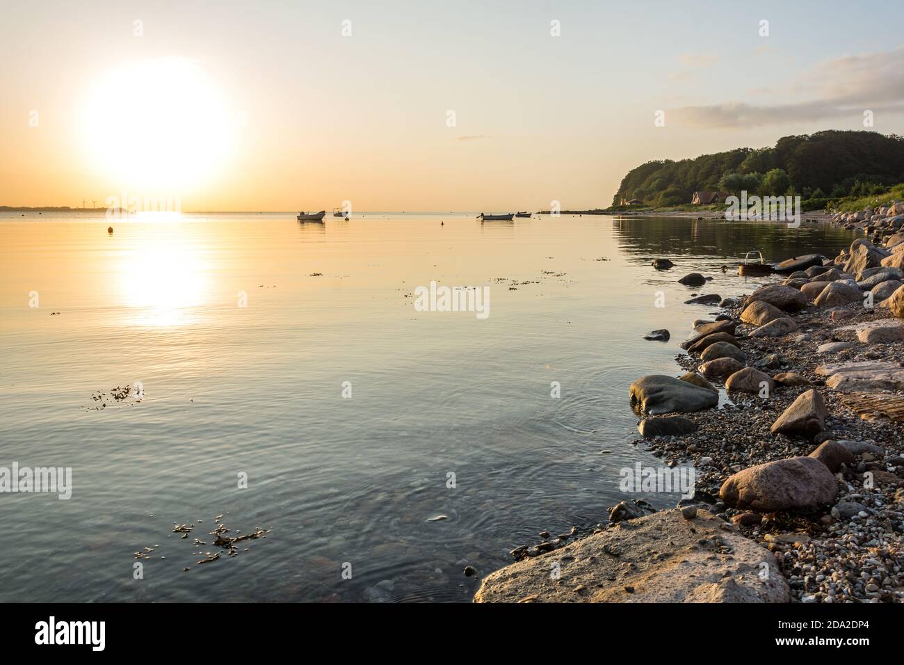 Beautiful sunrise over peaceful bay at the Baltic Sea with small boats and rocky shore Stock Photo