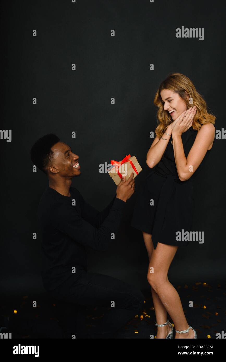 A young black man proposes to his Caucasian girlfriend while standing on one knee. Multi-ethnic couple. Stock Photo