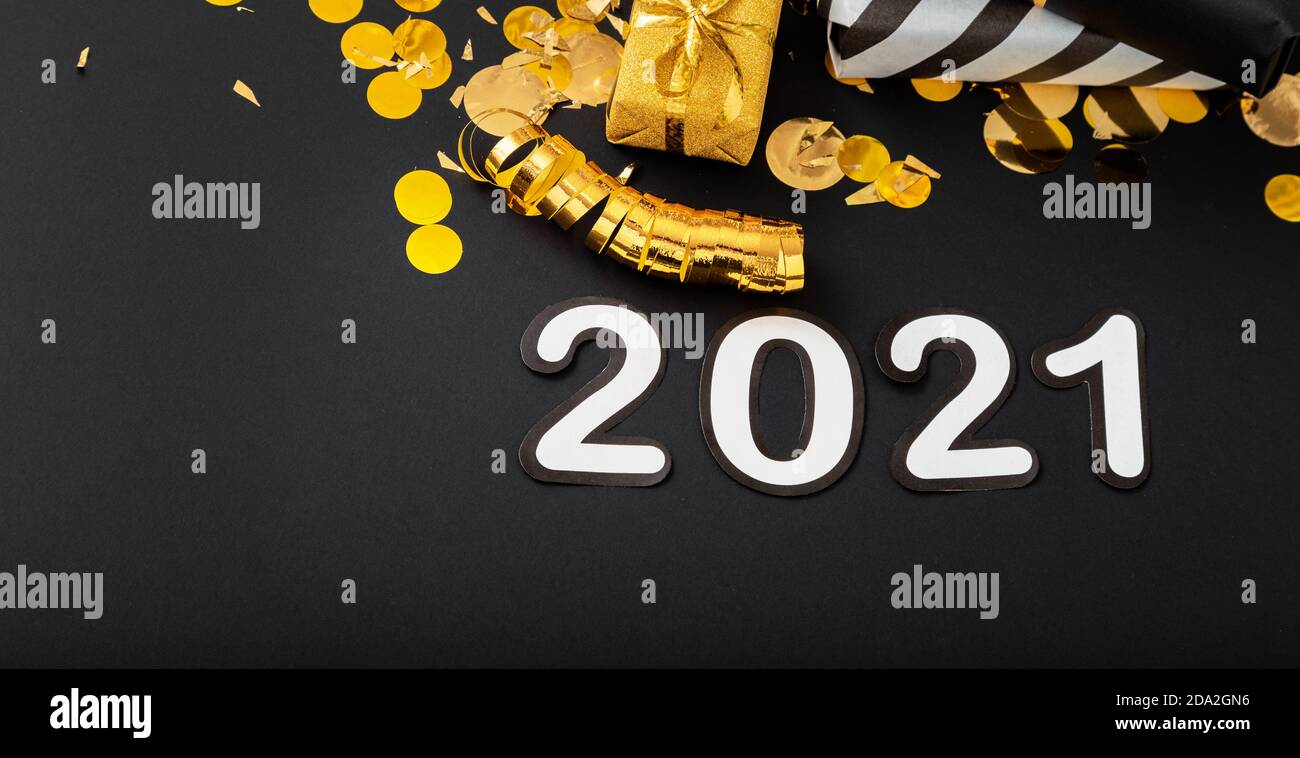 2021 white text lettering on black background with golden confetti, Christmas gift boxes gold balls festive decor. Happy New year event composition. L Stock Photo