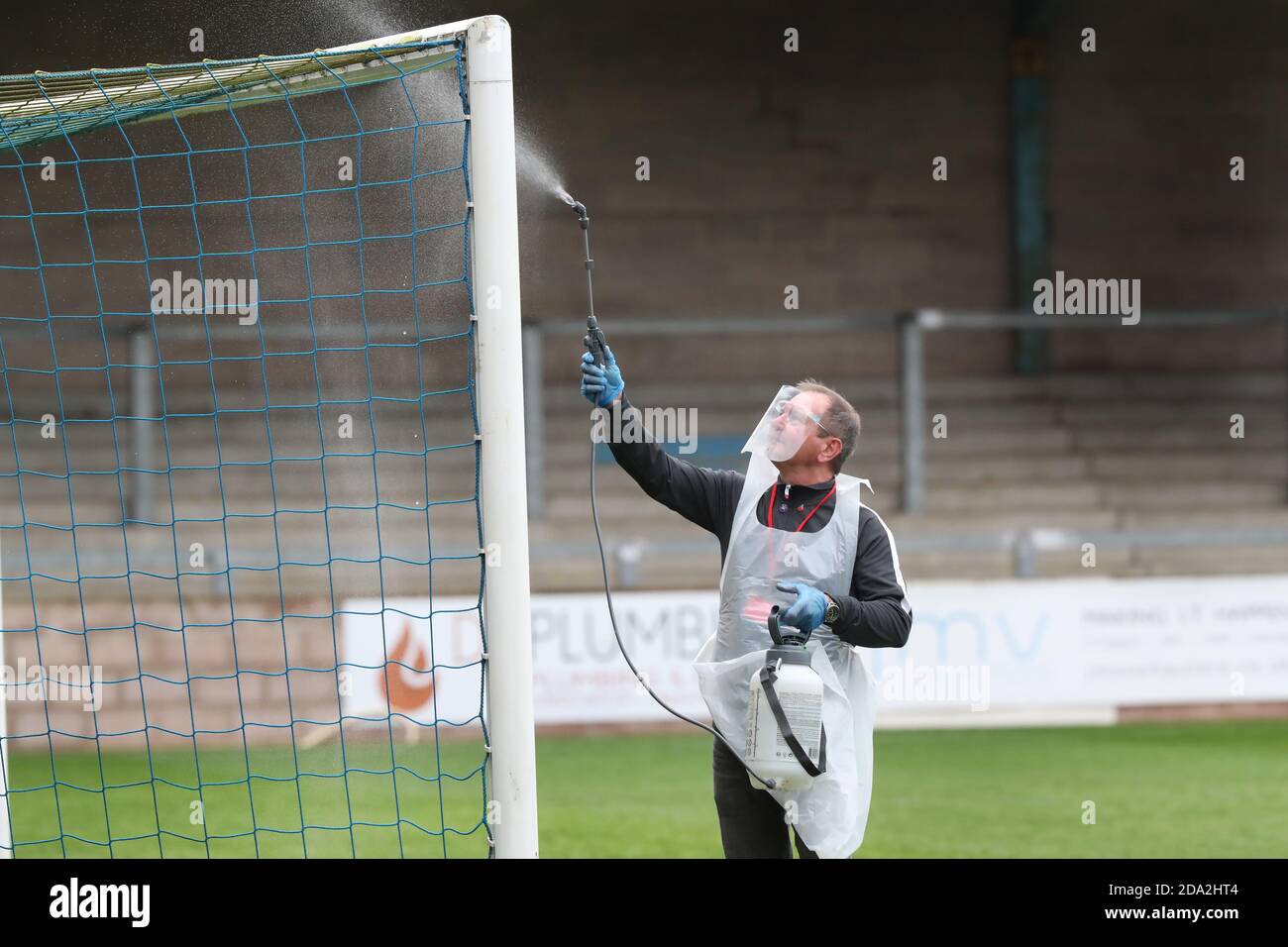 A official wearing PPE sprays the goal posts with disinfectant spray before the First round of the Emirates FA Cup between Torquay United and Crawley Town at Plainmoor, Torquay.  Picture James Boardman / Telephoto Images Stock Photo