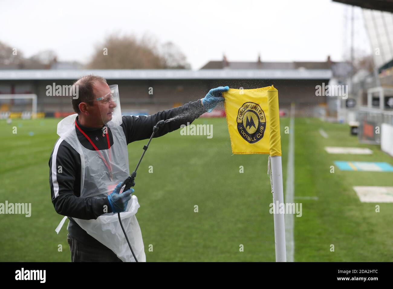 A official wearing PPE sprays the corner flag with disinfectant spray before the First round of the Emirates FA Cup between Torquay United and Crawley Town at Plainmoor, Torquay.  Picture James Boardman / Telephoto Images Stock Photo