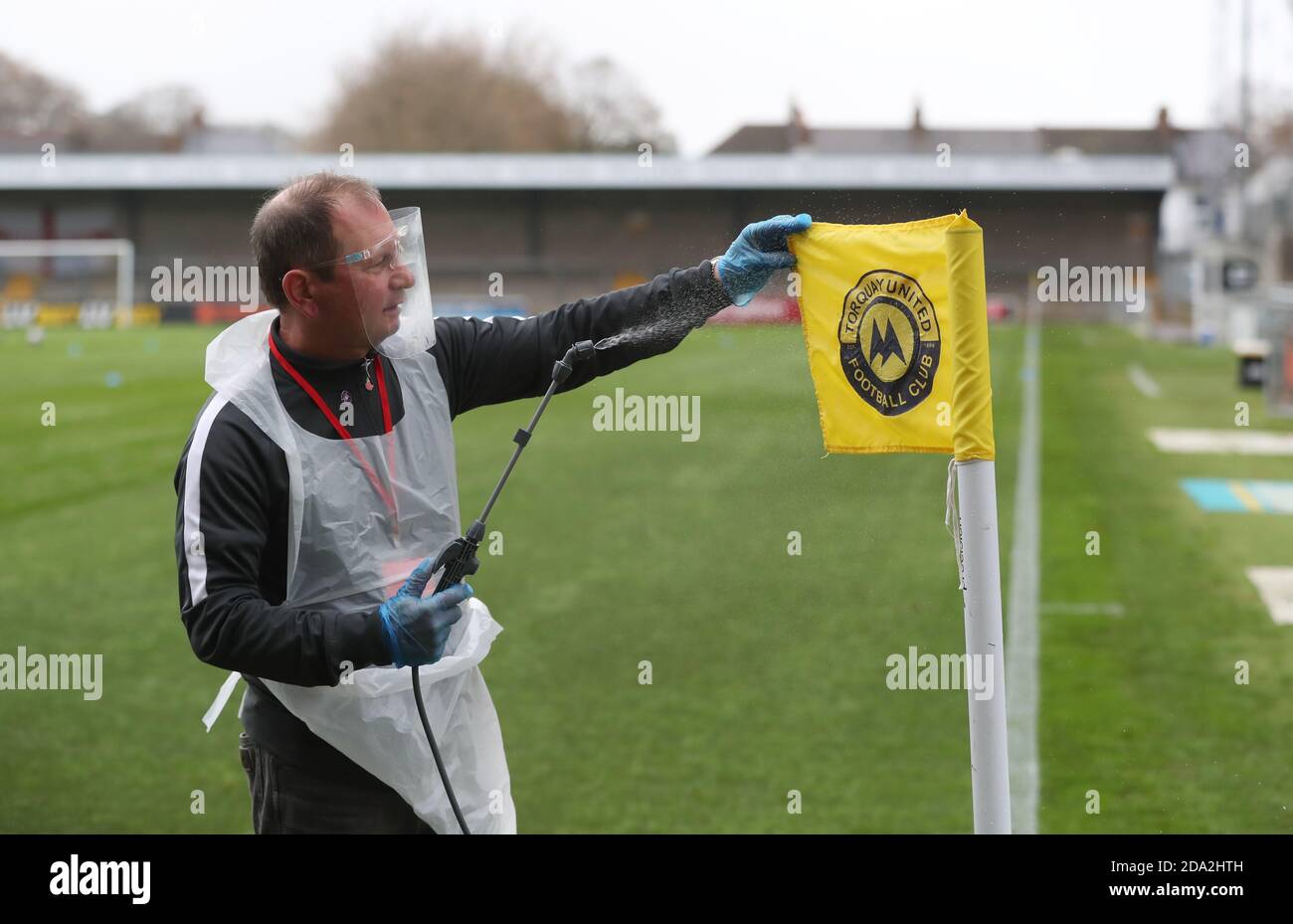 A official wearing PPE sprays the corner flag with disinfectant spray before the First round of the Emirates FA Cup between Torquay United and Crawley Town at Plainmoor, Torquay.  Picture James Boardman / Telephoto Images Stock Photo