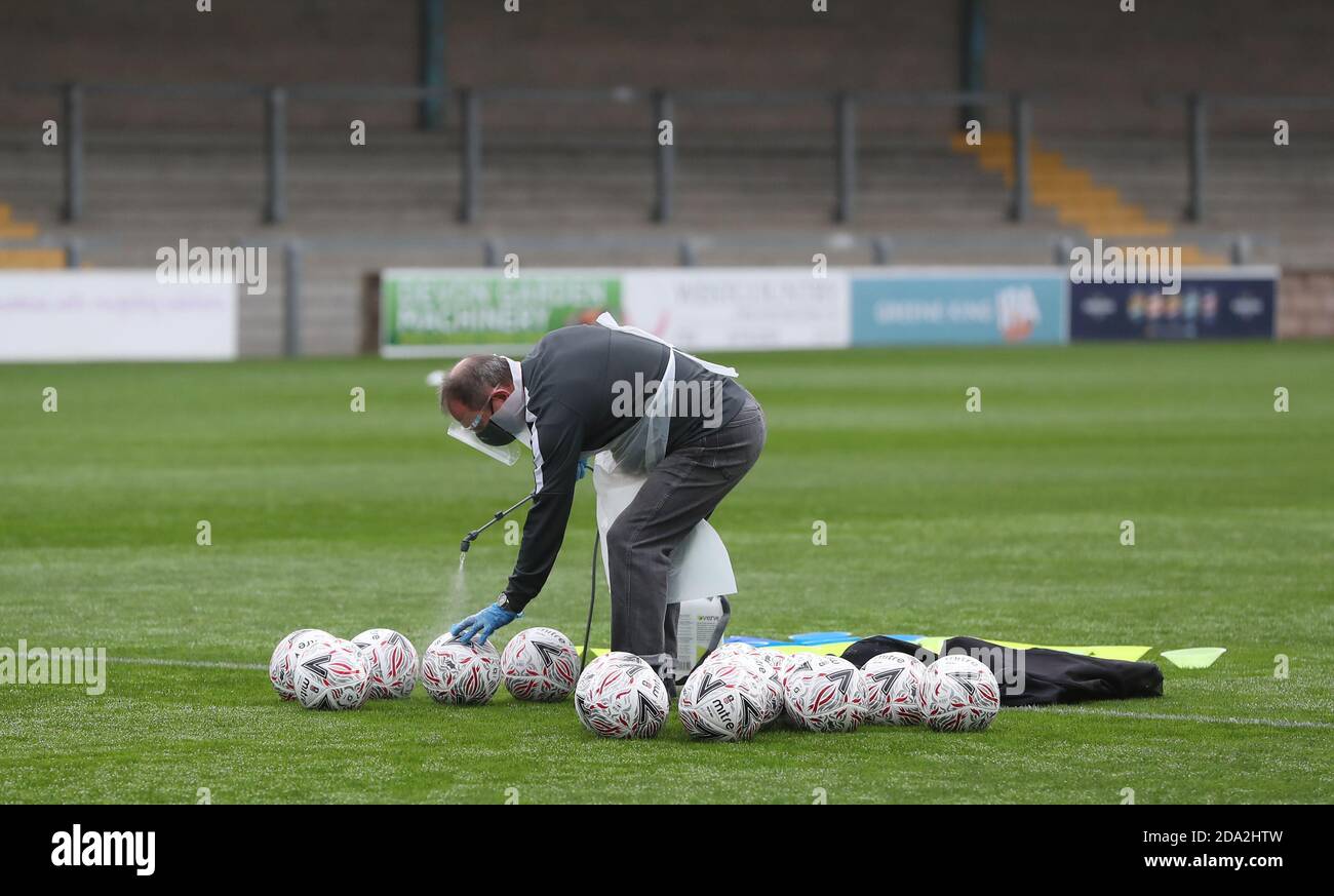 A official wearing PPE sprays footballs with disinfectant spray before the First round of the Emirates FA Cup between Torquay United and Crawley Town at Plainmoor, Torquay.  Picture James Boardman / Telephoto Images Stock Photo