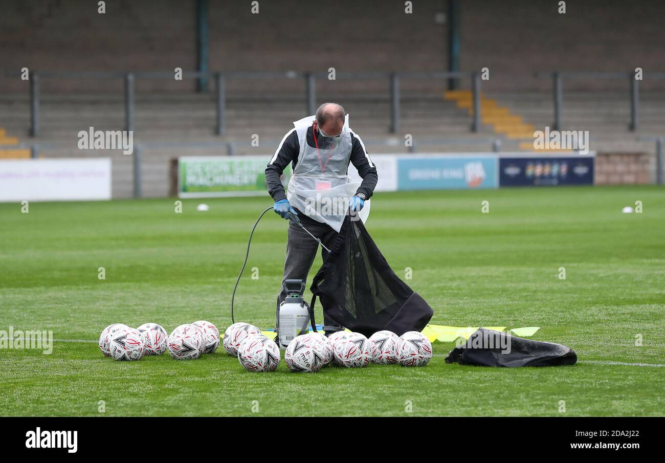 A official wearing PPE sprays footballs with disinfectant spray before the First round of the Emirates FA Cup between Torquay United and Crawley Town at Plainmoor, Torquay.  Picture James Boardman / Telephoto Images Stock Photo