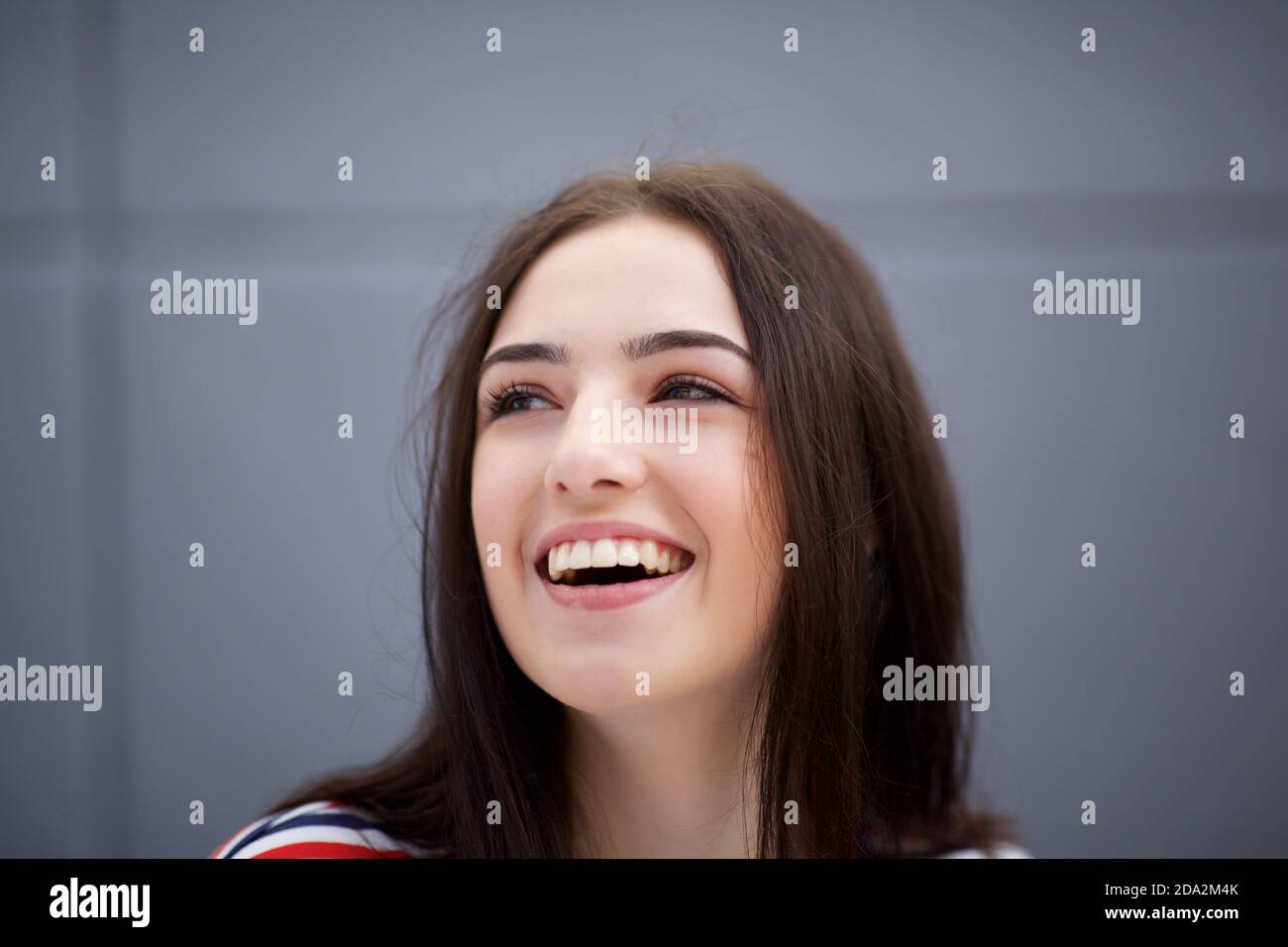 Close up portrait of beautiful young woman smiling against gray ...