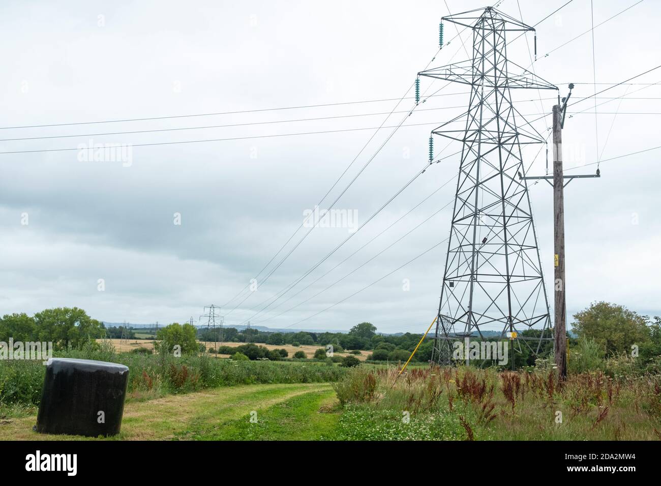 Rural landscape with silage bale and electricity pylon at the entrance to a farm field in southern England Stock Photo