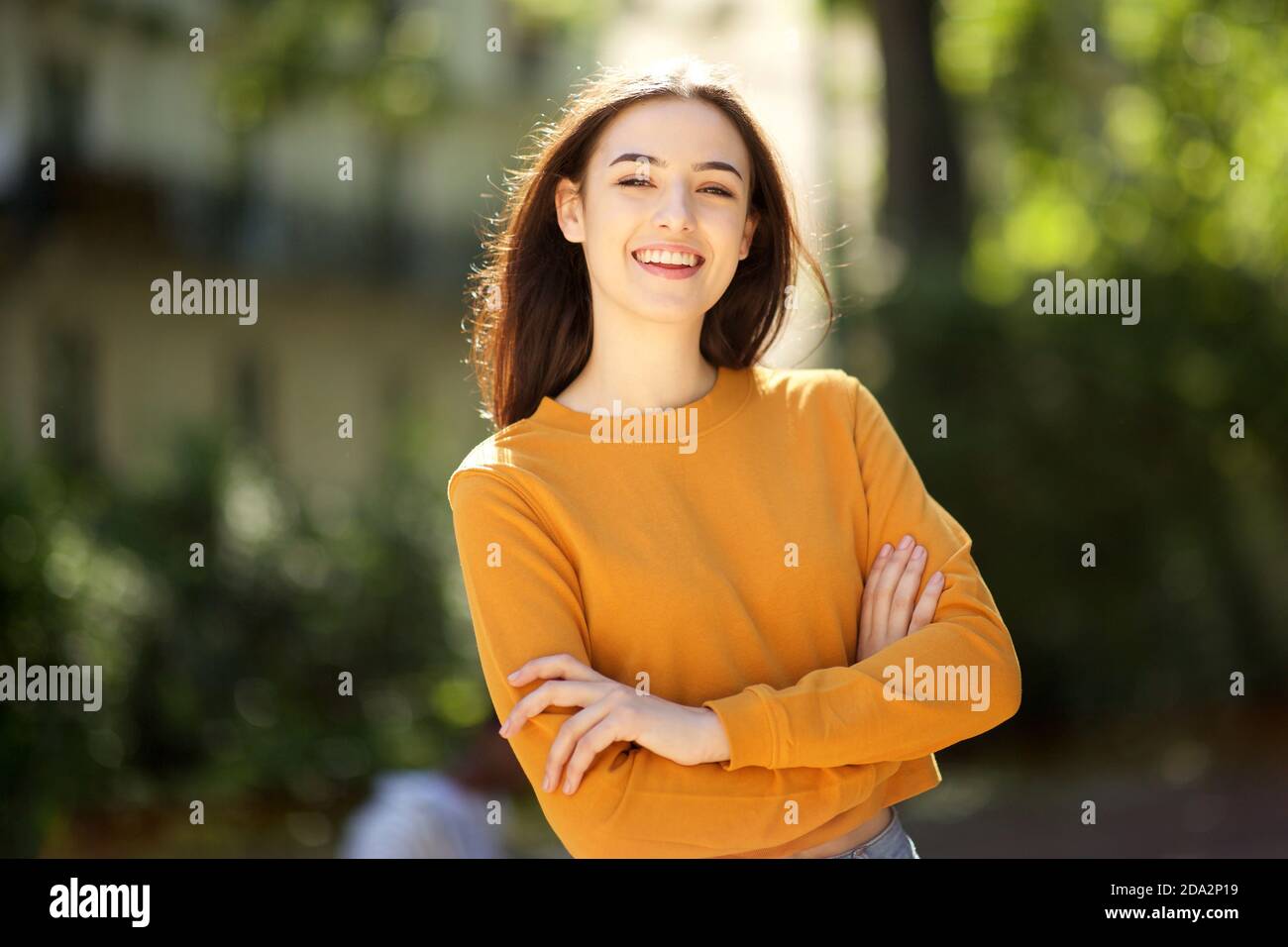 Portrait of smiling young woman with arms crossed in the park Stock ...