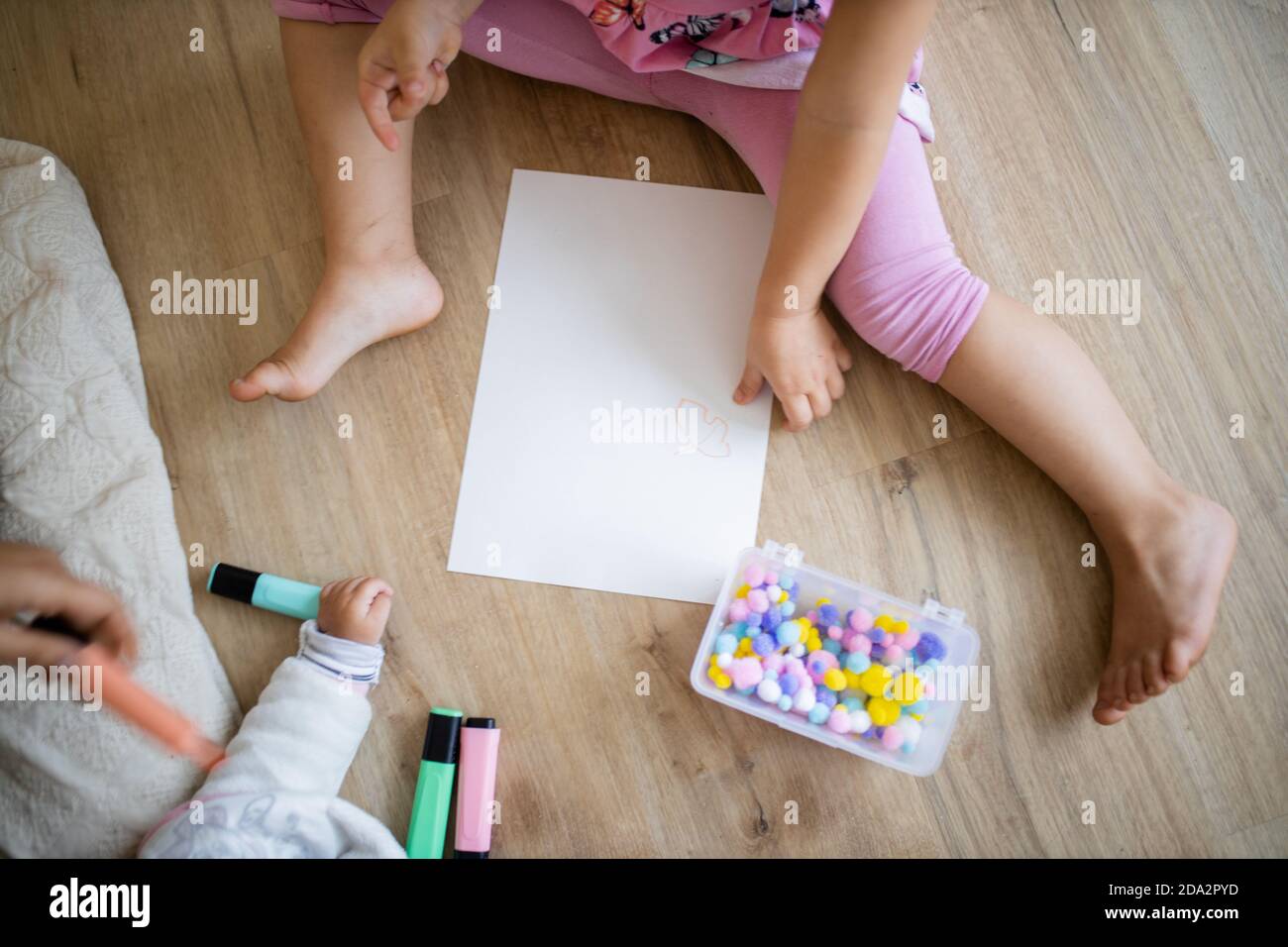 Little girl sitting on the wooden floor with a paper sheet and cotton balls Stock Photo