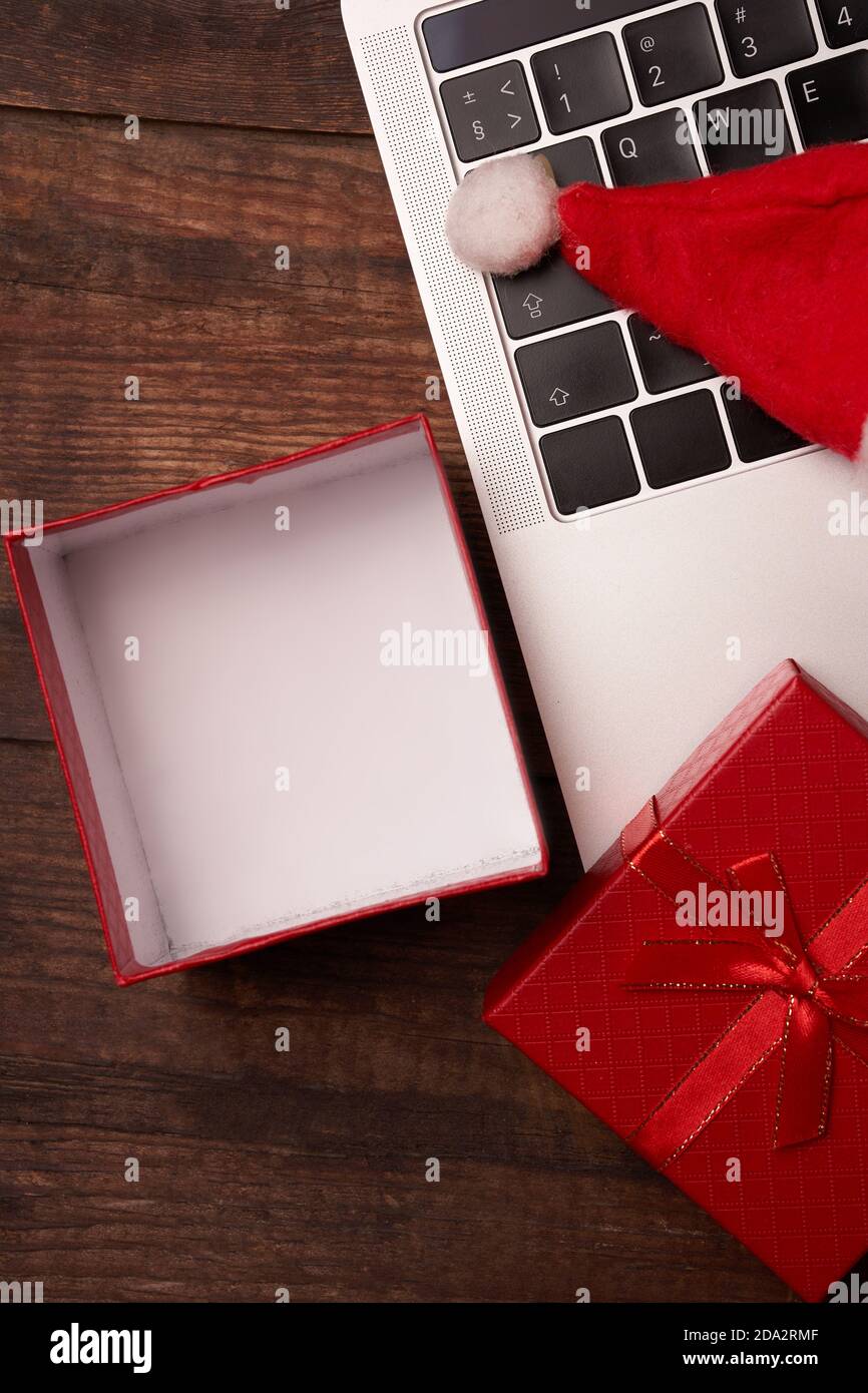 Online shopping for Christmas, a laptop stands on a wooden table next to an open box, with space for your gift, and a Christmas cap Stock Photo