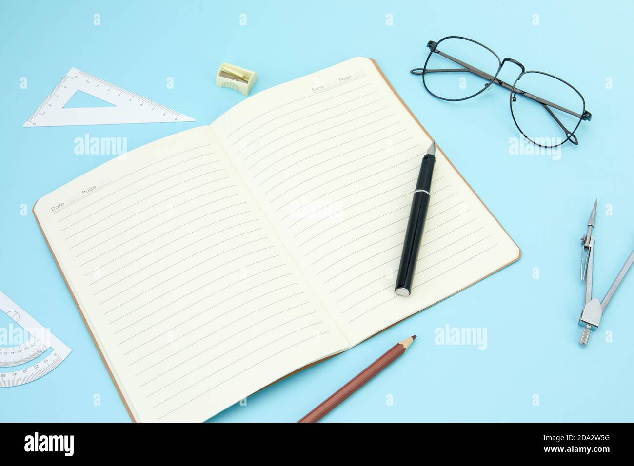 Open notebook, ballpen, pencil, sharpener, rulers, and eyeglasses isolated on a blue surface Stock Photo