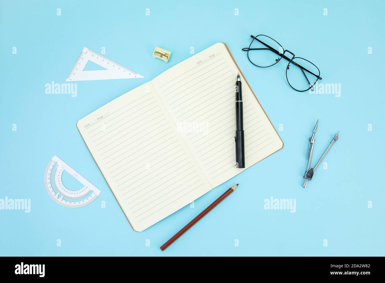 Open notebook, ballpen, pencil, sharpener, rulers, and eyeglasses isolated on a blue surface Stock Photo