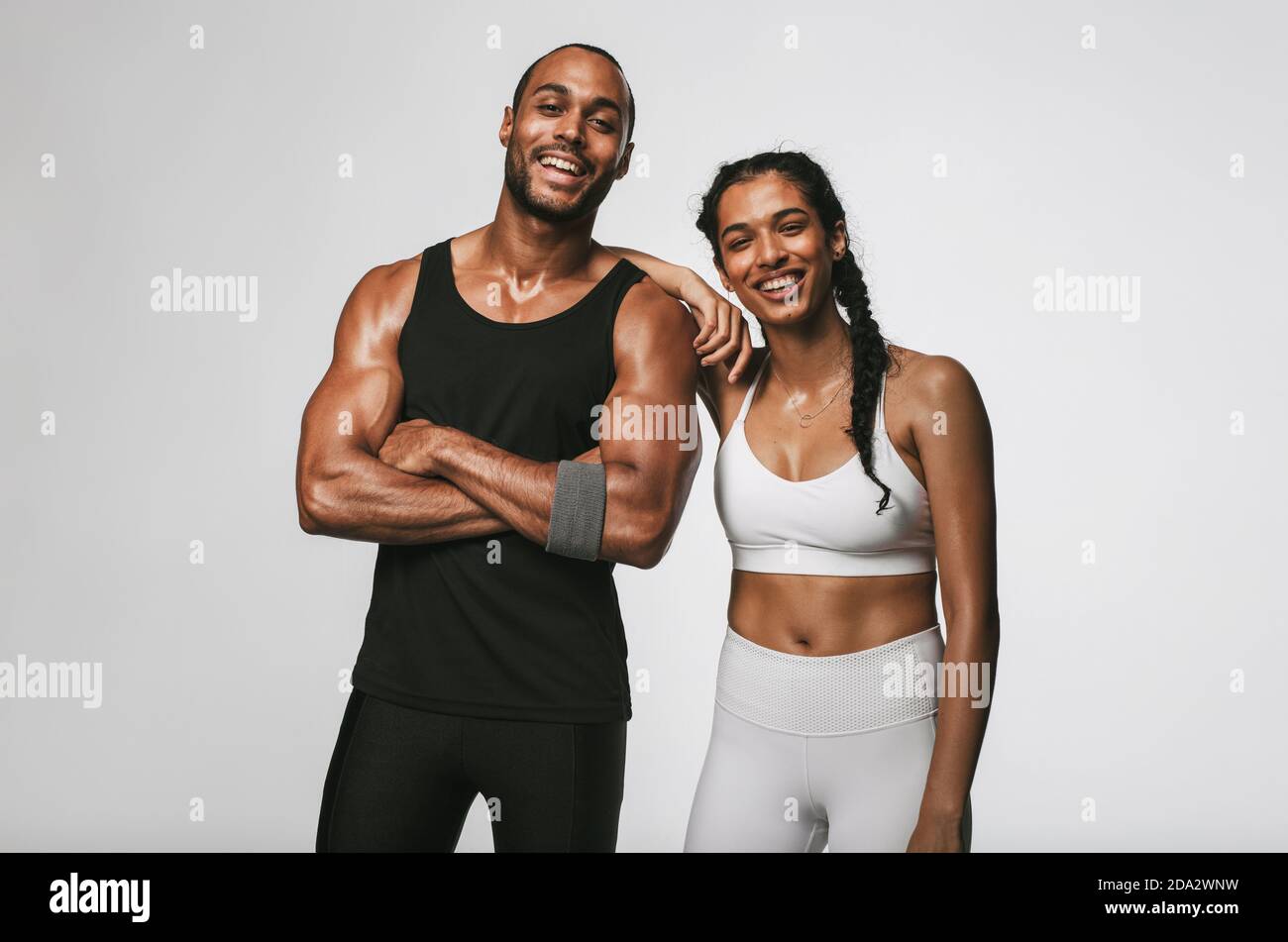 Cheerful male and female athlete standing together at gym. Smiling woman standing with her hand on shoulder of male friend. Stock Photo