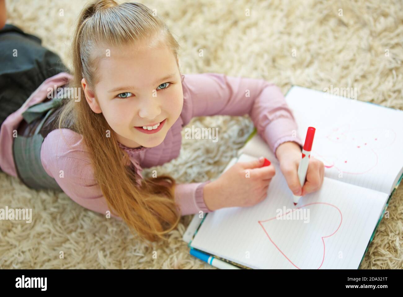 Girl paints a big red heart in her exercise book Stock Photo
