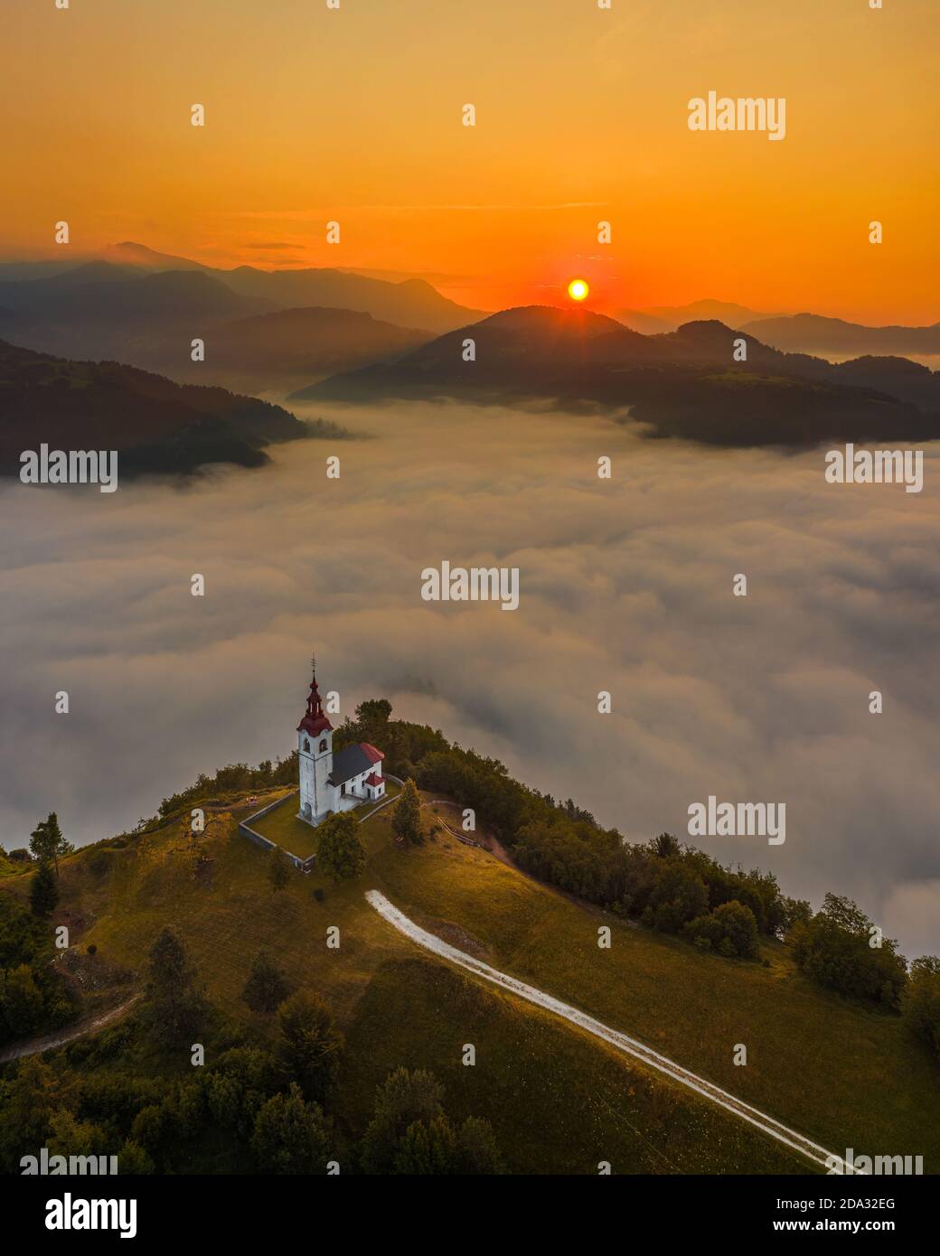 Sebrelje, Slovenia - Aerial drone view of the beautiful hilltop church of St.Ivan (Sv. Ivan Cerkev) at sunrise with huge morning fog bellow and Julian Stock Photo