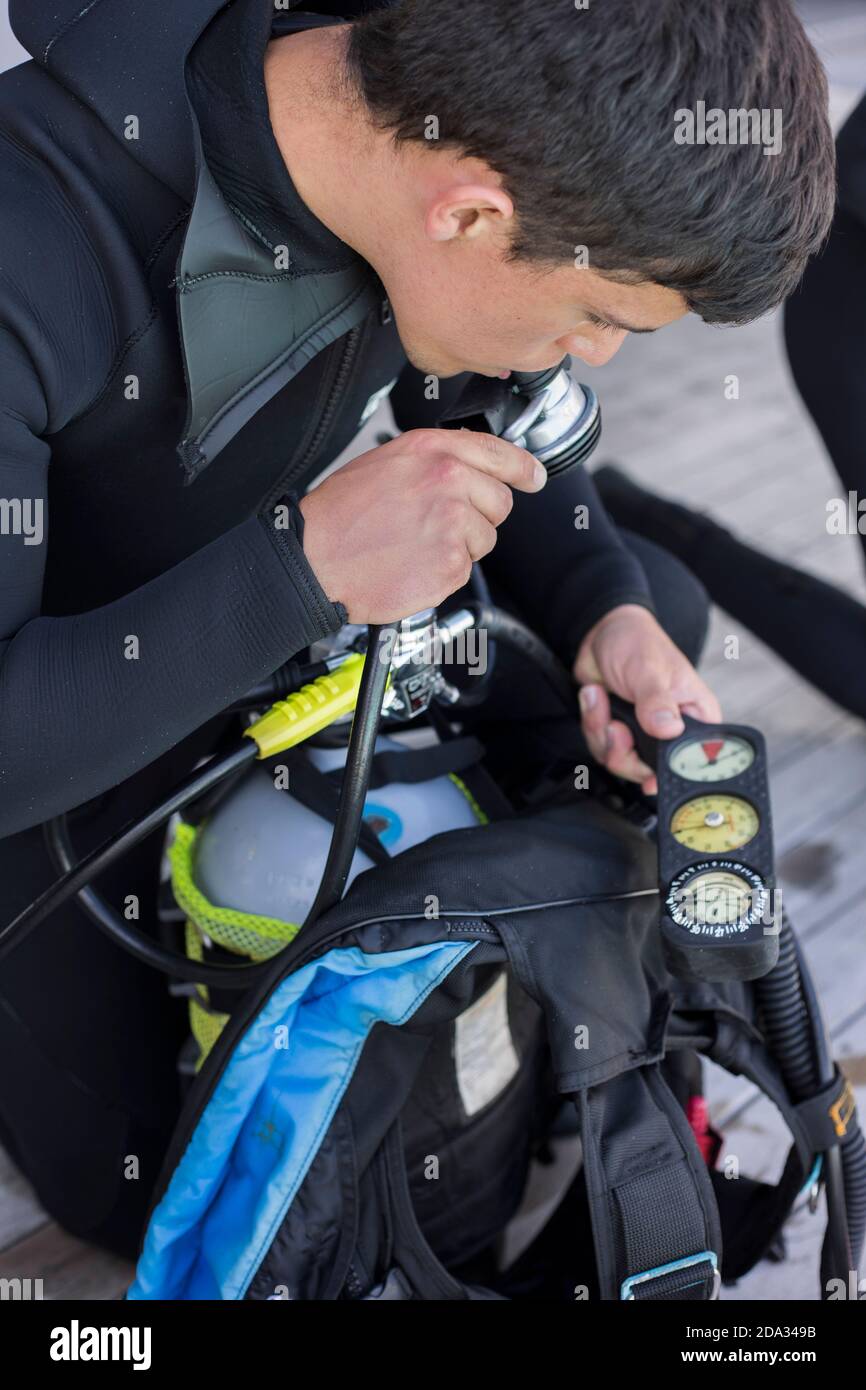 Scuba diver kitting up and checking his gear, testing regulator and