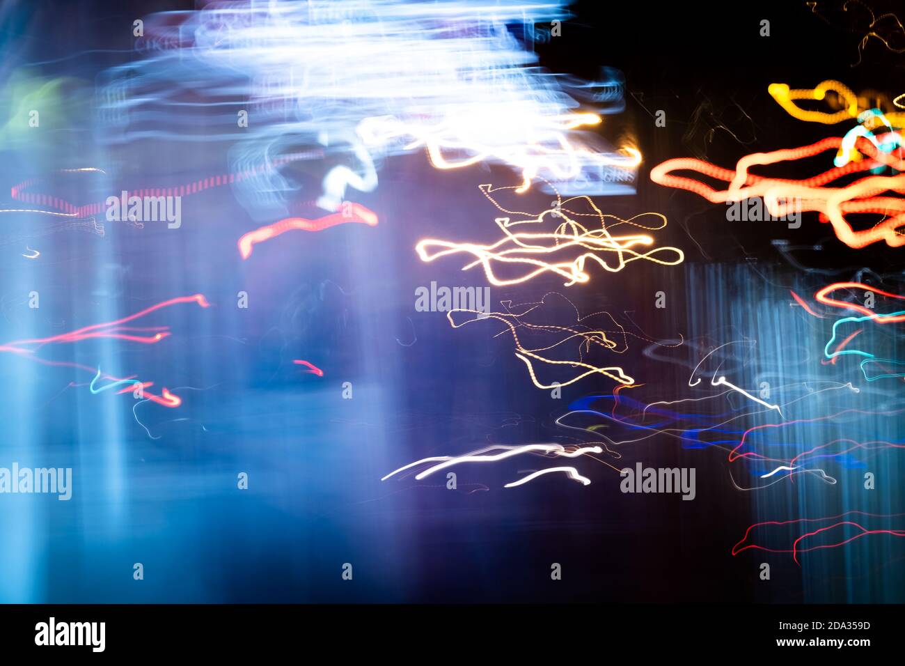Long exposure light painting photography, curvy lines of vibrant neon metallic yellow-orange blue colors against a black background. Stock Photo