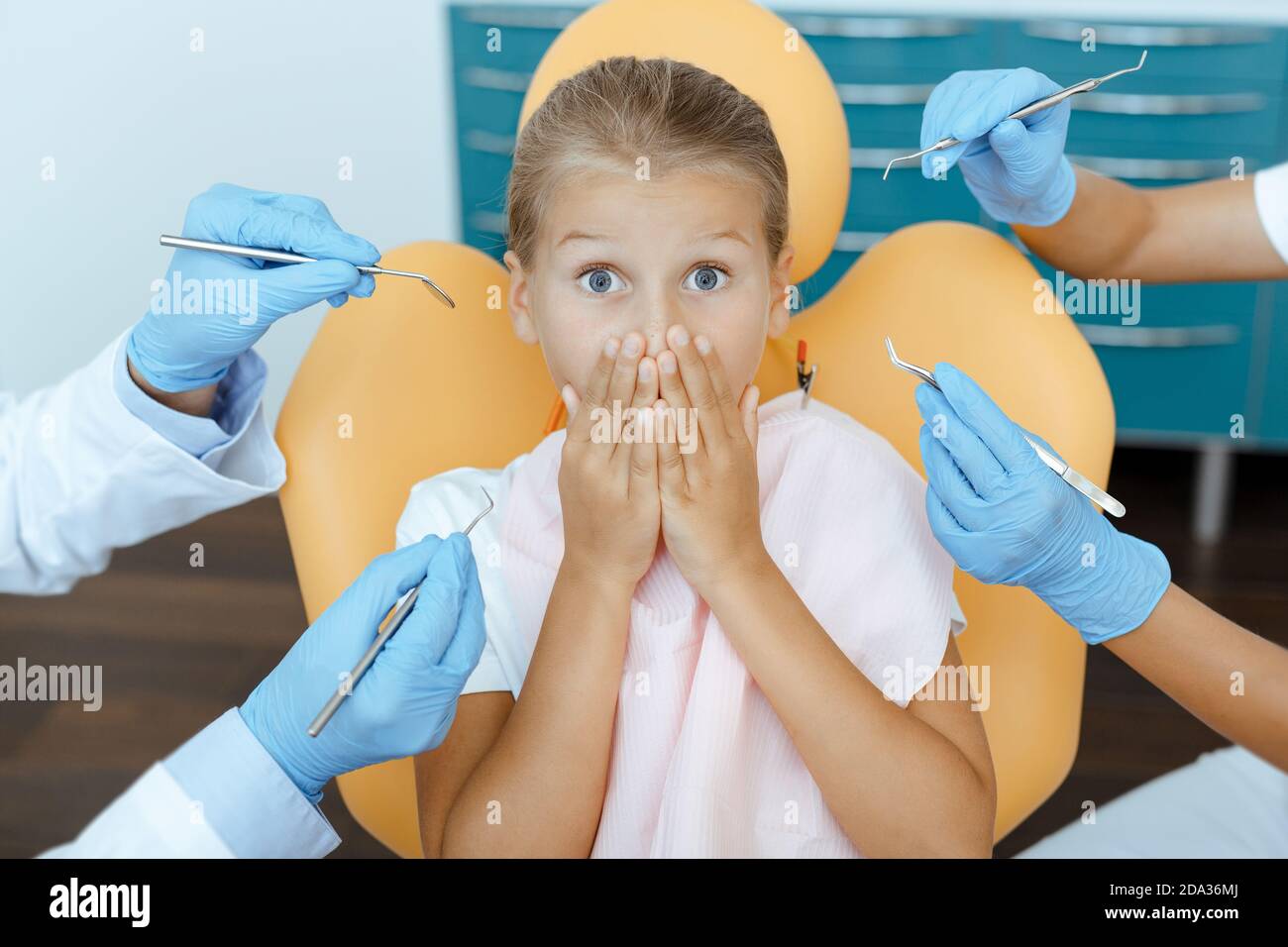 Scared girl with wide open eyes covers mouth with hands and sits in chair Stock Photo