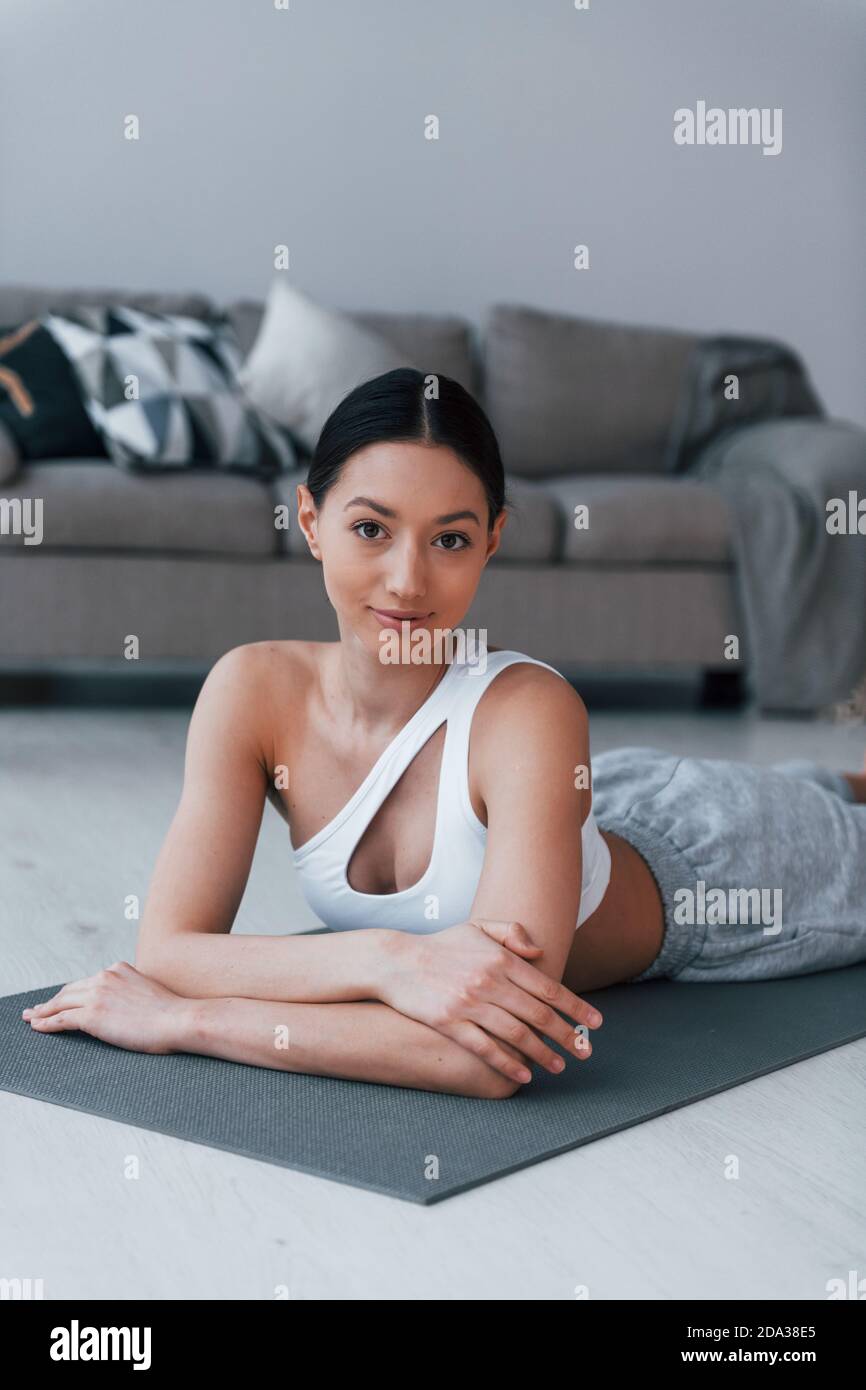 Lying down on the mat and taking a break. Young woman with slim body shape in sportswear have fitness day indoors at home Stock Photo