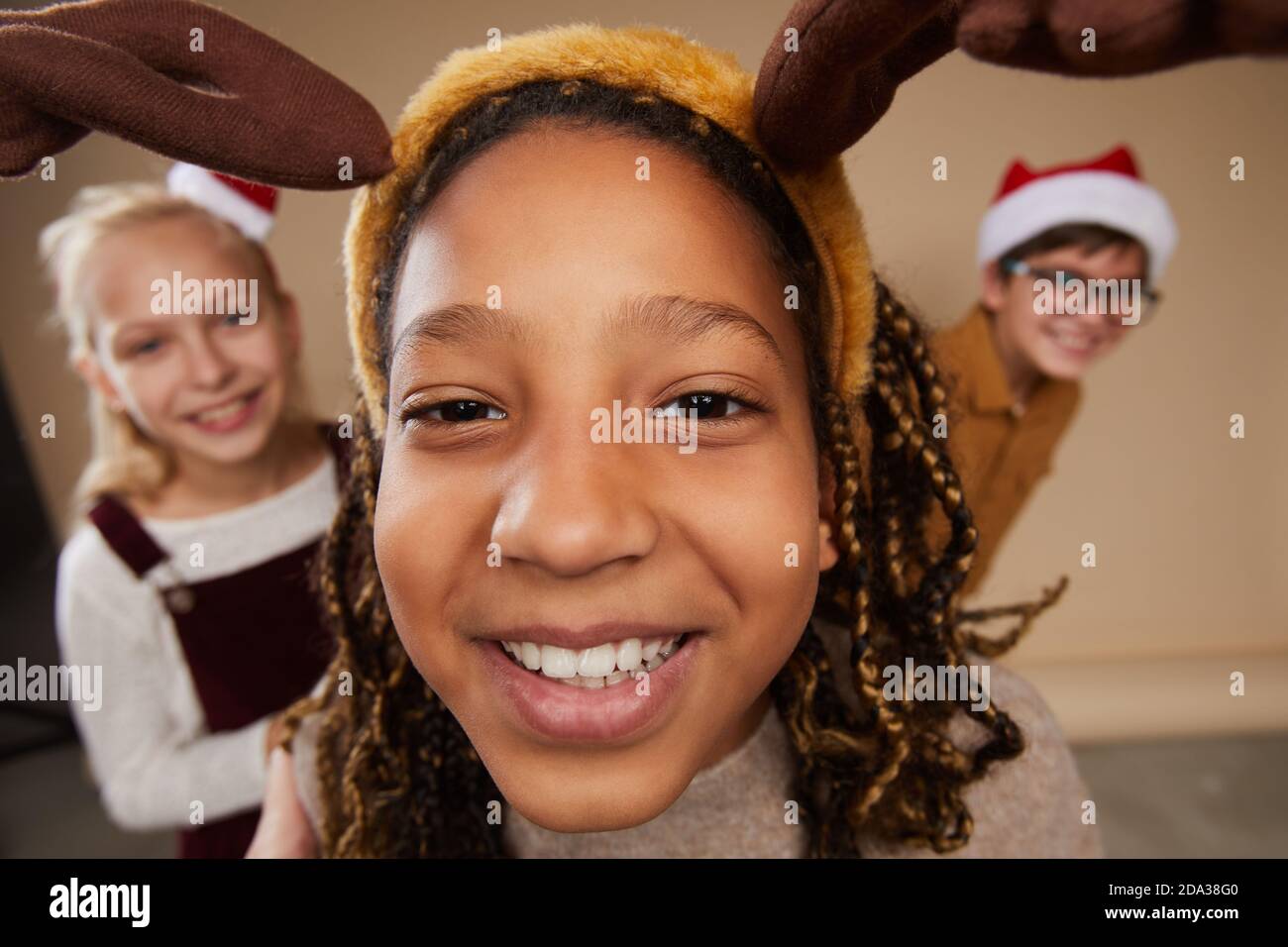 Fish eye portrait of three children wearing Christmas portraits and smiling at camera while standing against beinge background in studio Stock Photo