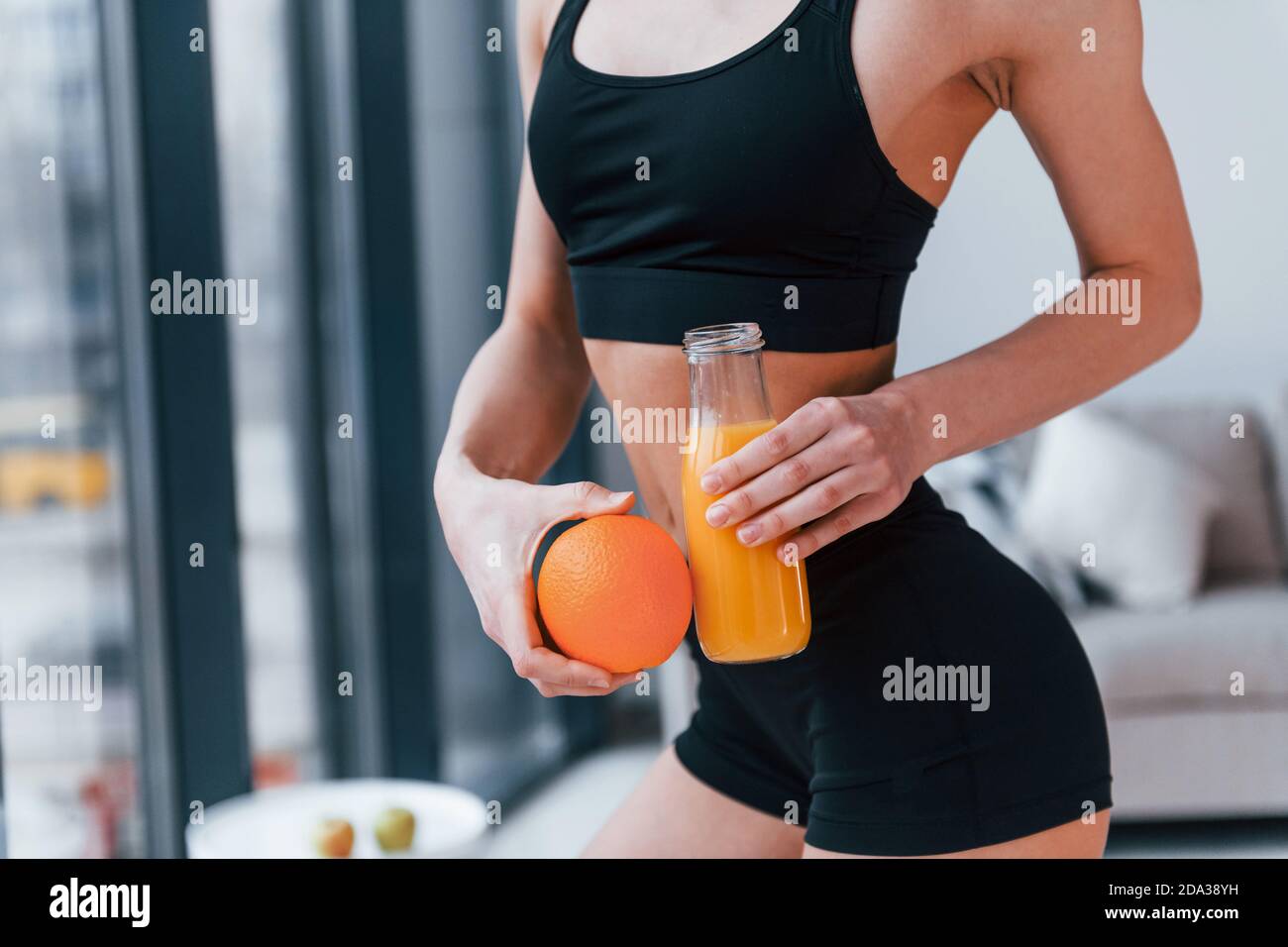 holds healthy food in hands. Young woman with slim body shape in black sportswear have fitness day indoors at home Stock Photo