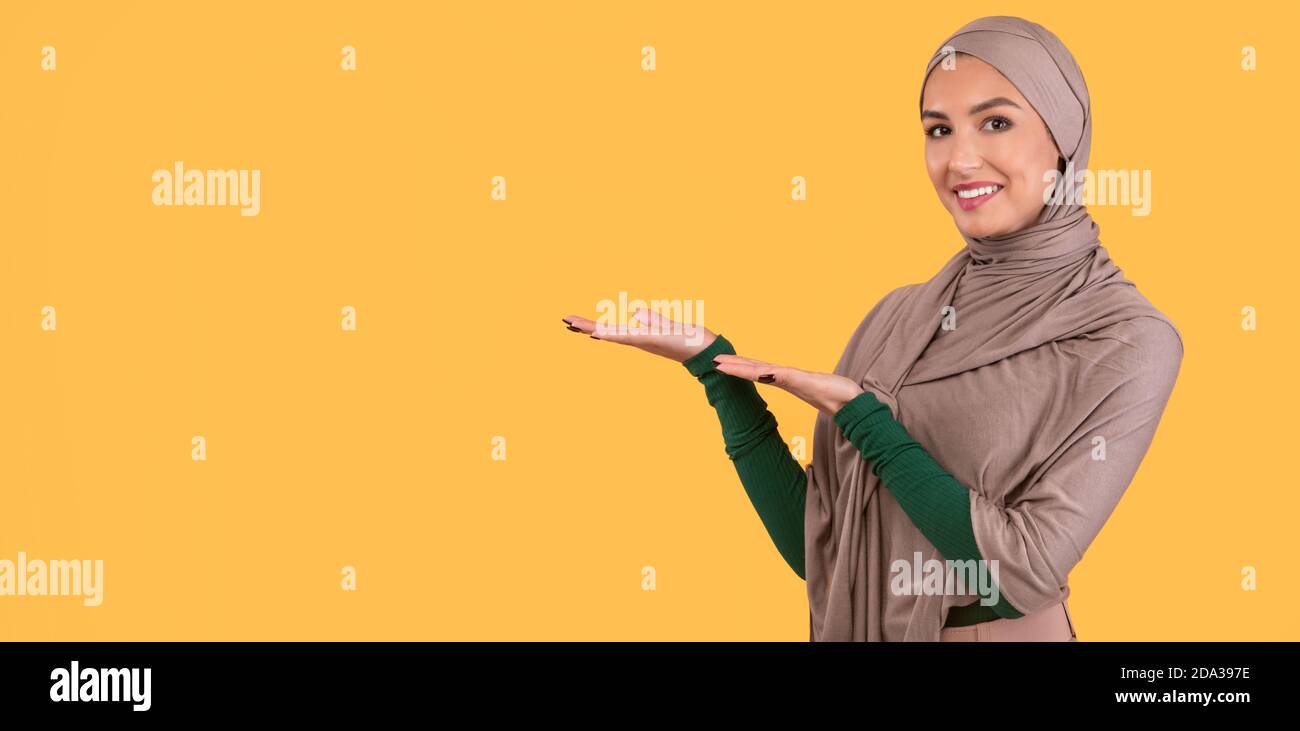 Muslim Woman In Hijab Showing Copy Space Aside, Yellow Background Stock