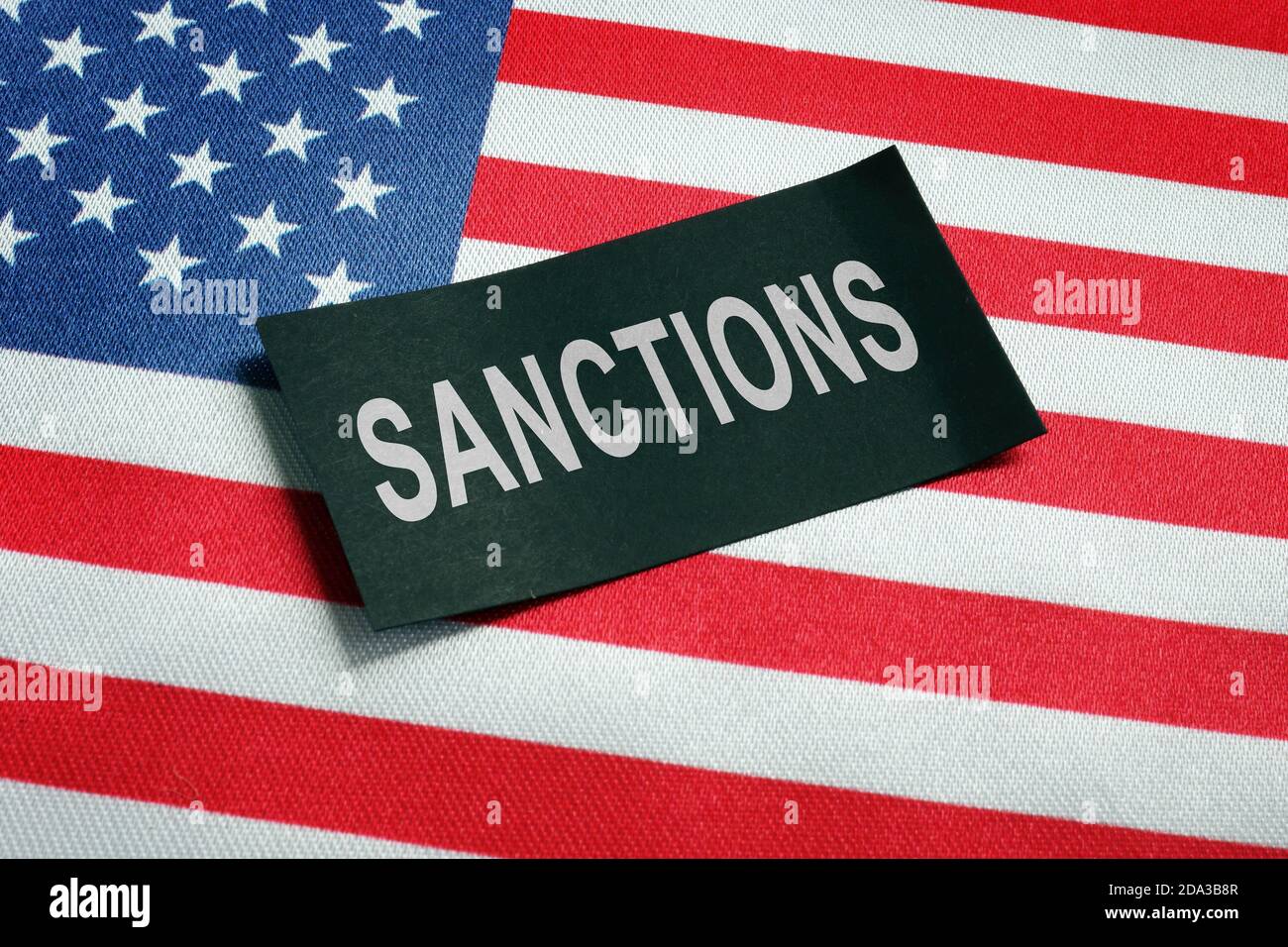 USA flag and word sanctions on the black piece of paper. Stock Photo