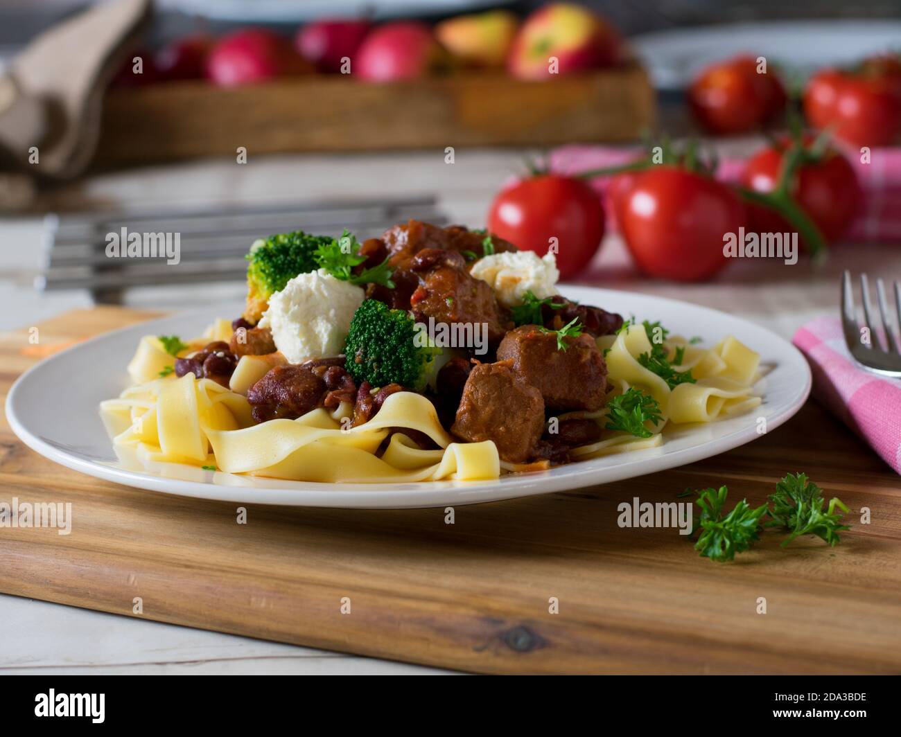 delicious pork bean goulash with sour cream topping and pasta on a plate Stock Photo