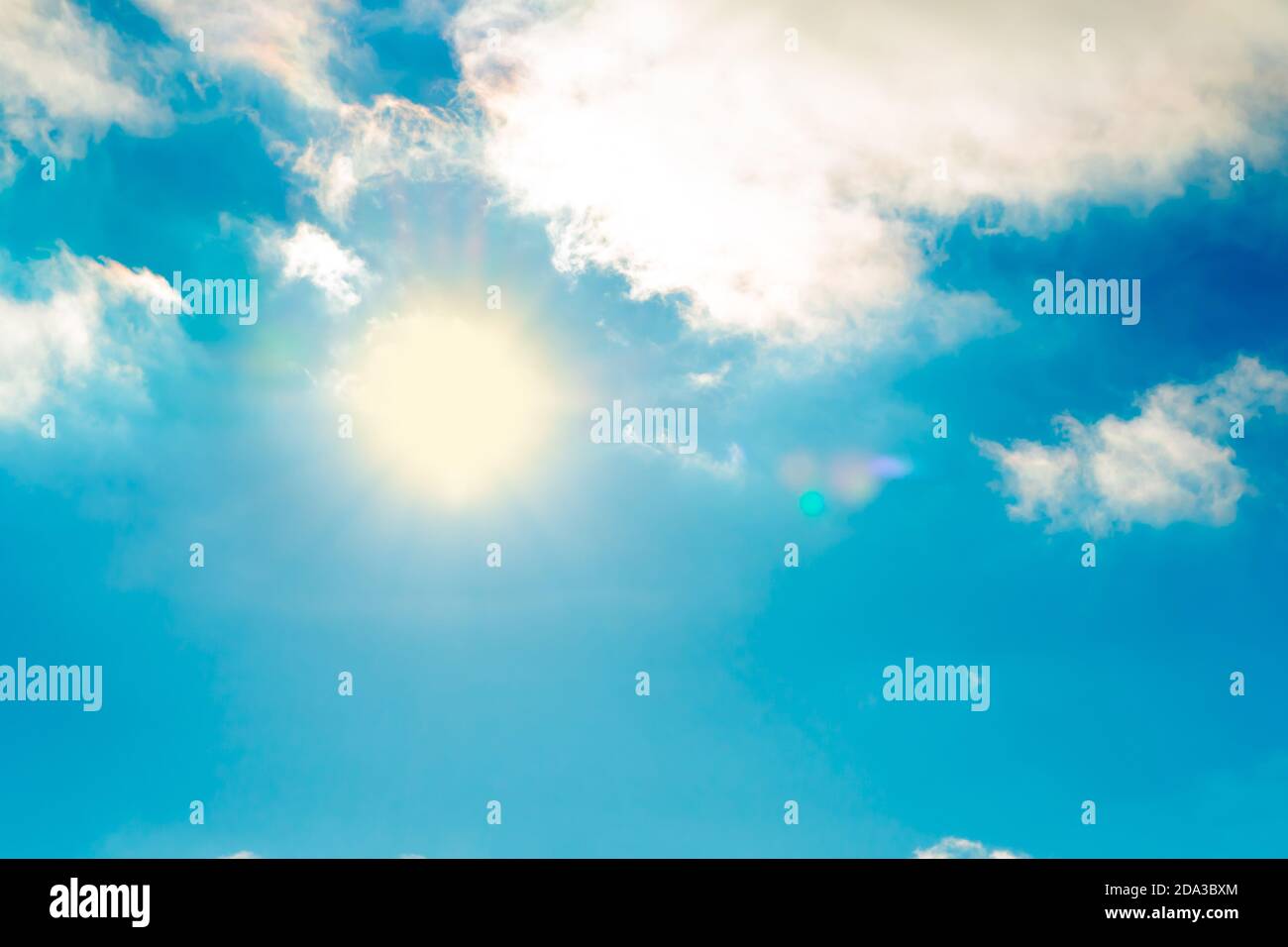 The sun in the blue sky under the clouds. Sunny day. Blue sky. Bright midday sun illuminates the space. Blue sky with clouds and sun reflection. The s Stock Photo