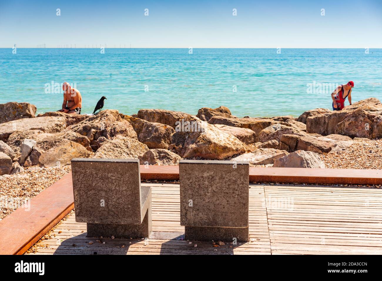 seaside landscape with blue sky on a summers days with male figure sitting on rocks with crow Stock Photo