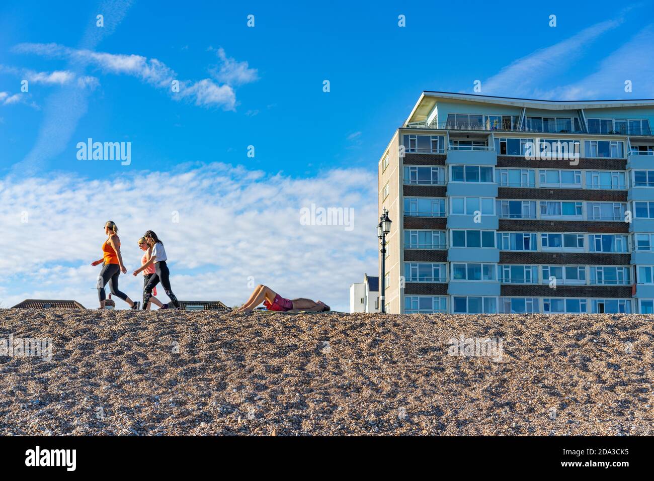 seaside landscape with male sunbather and a group of young people walking by on a summers days in Worthing. Stock Photo