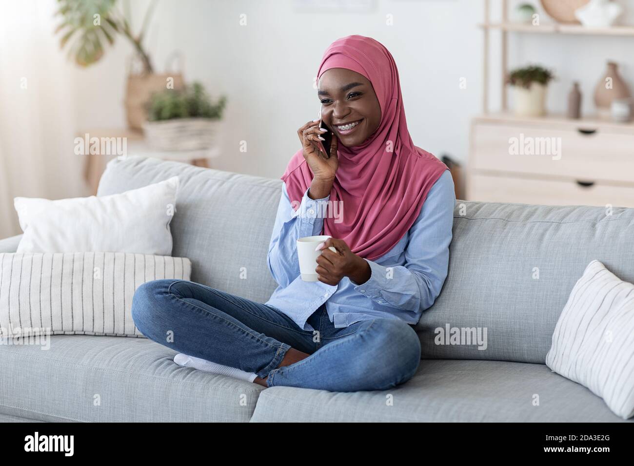 Black Muslim Woman Relaxing On Couch At Home With Smartphone And Coffee ...