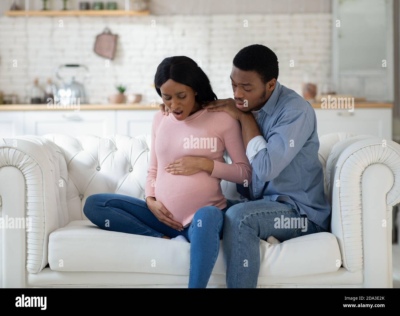Pregnant black woman feeling pain, giving birth to child, having contractions while husband calling doctor on phone Stock Photo