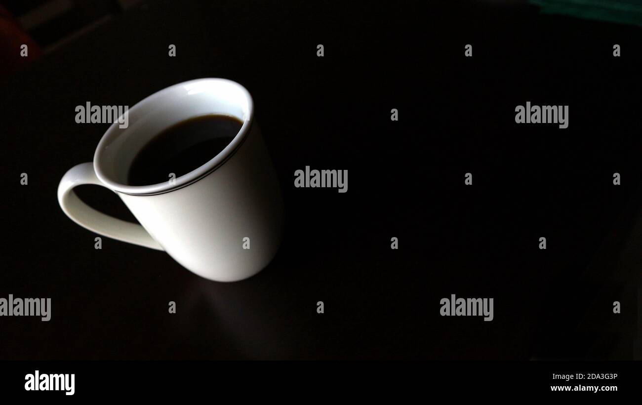 Angled white mug with black coffee on black background Stock Photo