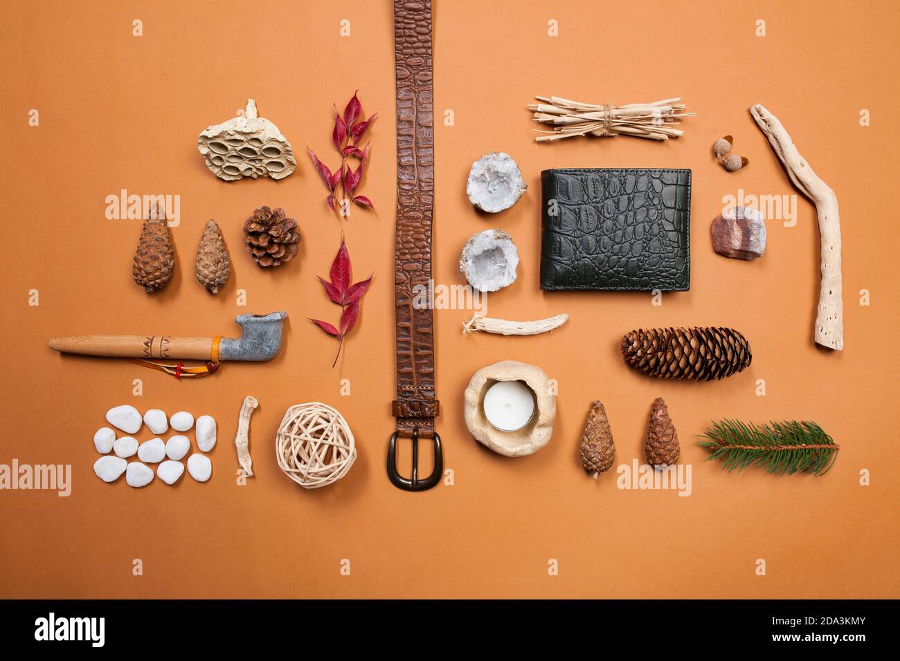 Still life composition of belt, wallet, peace pipe and natural things like pine cones, white stones, red leafs and minerals on a brown background Stock Photo