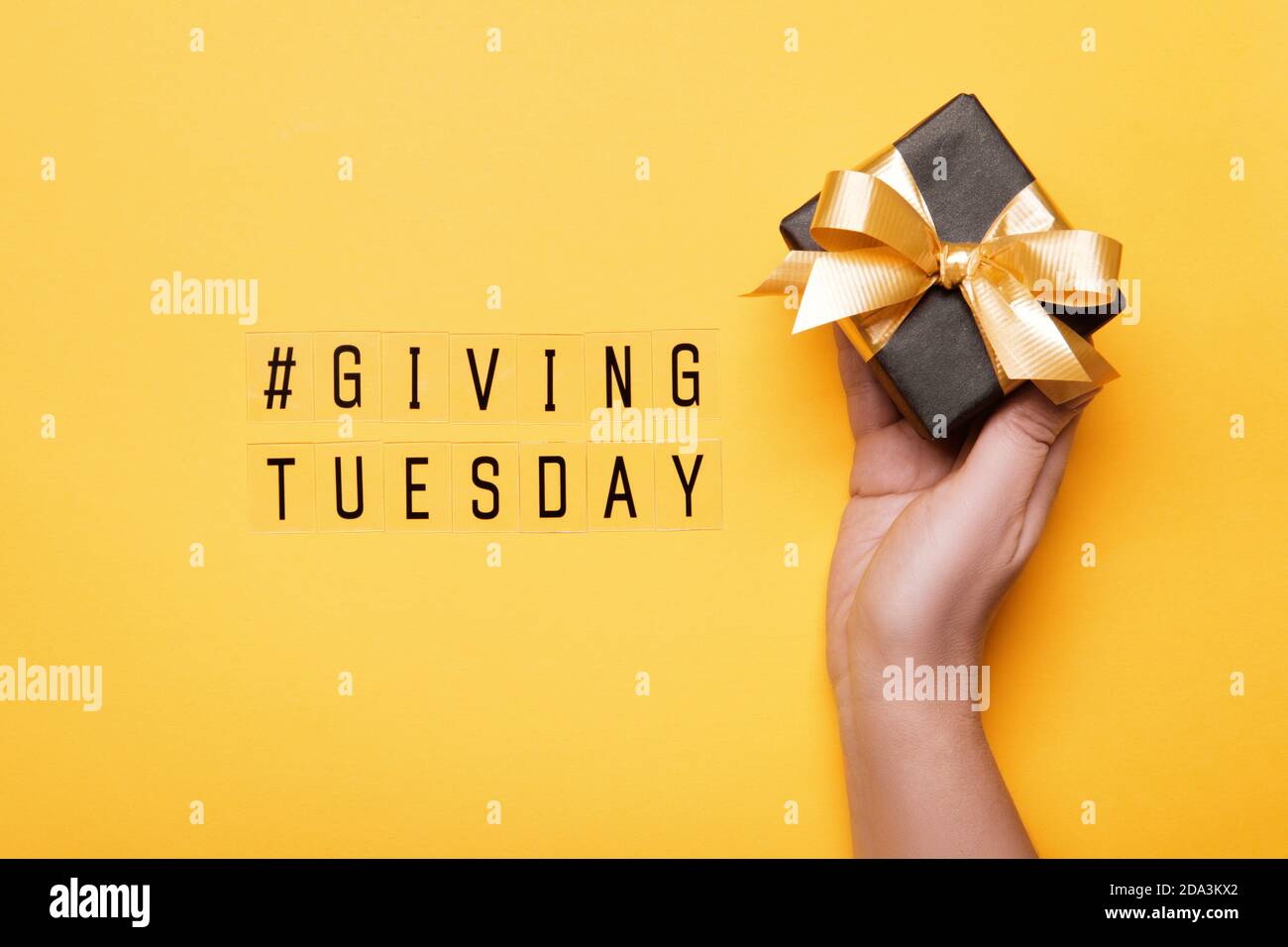 Giving Tuesday. Global day of charitable giving after Black Friday shopping day. Woman hand holding gift box on yellow background Stock Photo