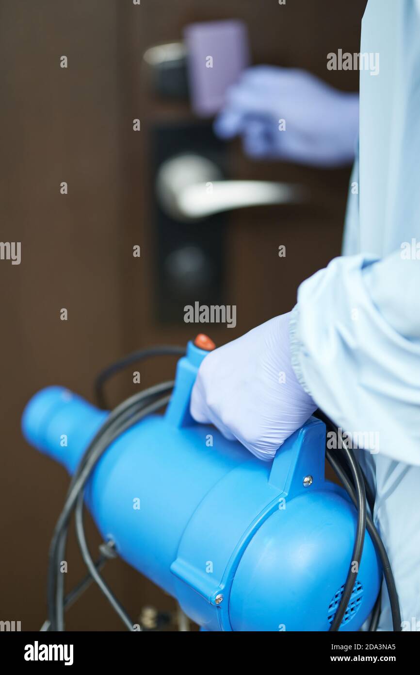 Close up of man protective blue suit opening hotel room and going to make disinfection. Coronavirus and quarantine concept. Focus on disinfectant Stock Photo