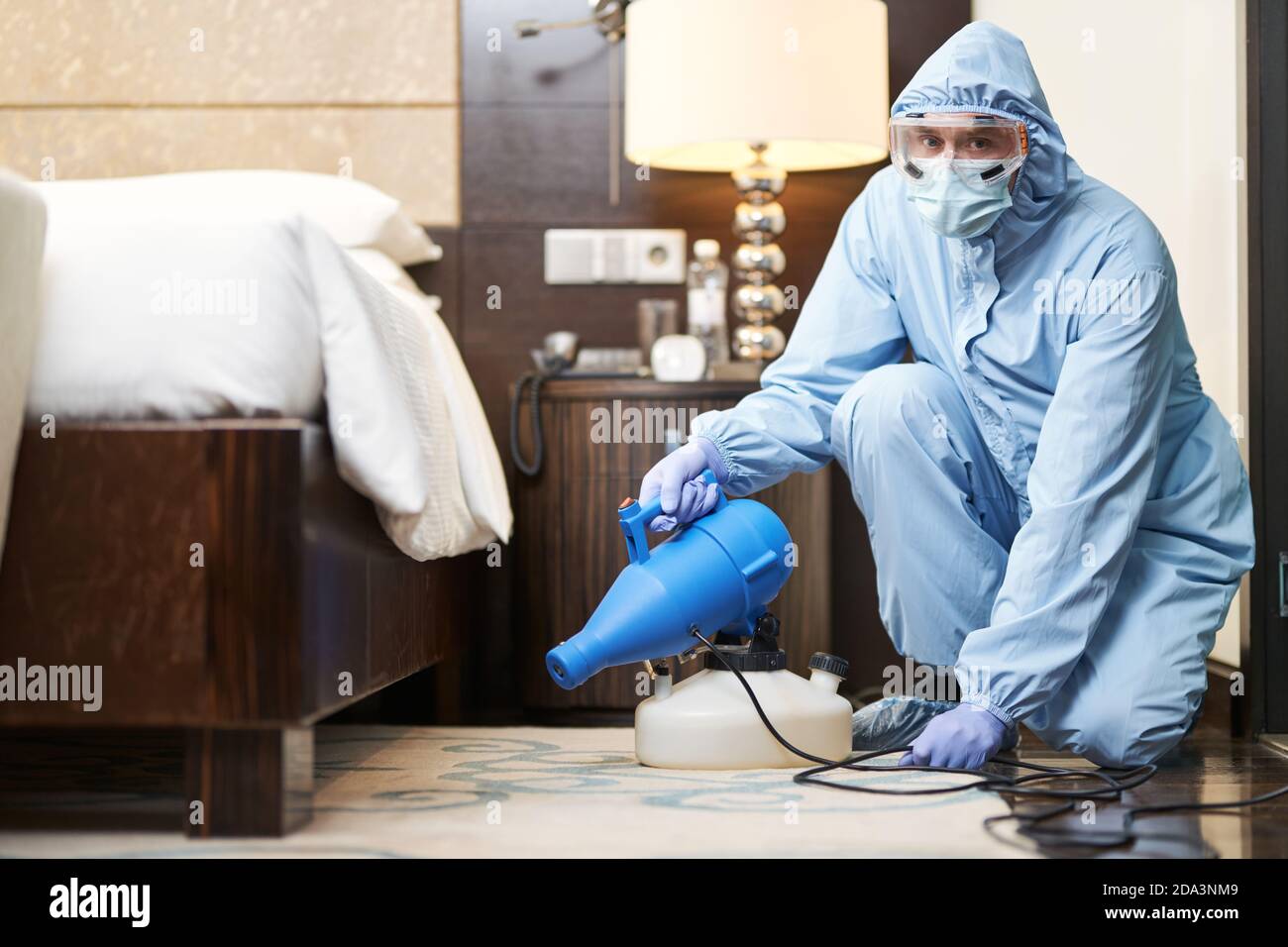 Man doing disinfection under the bed in a hotel room. Coronavirus and