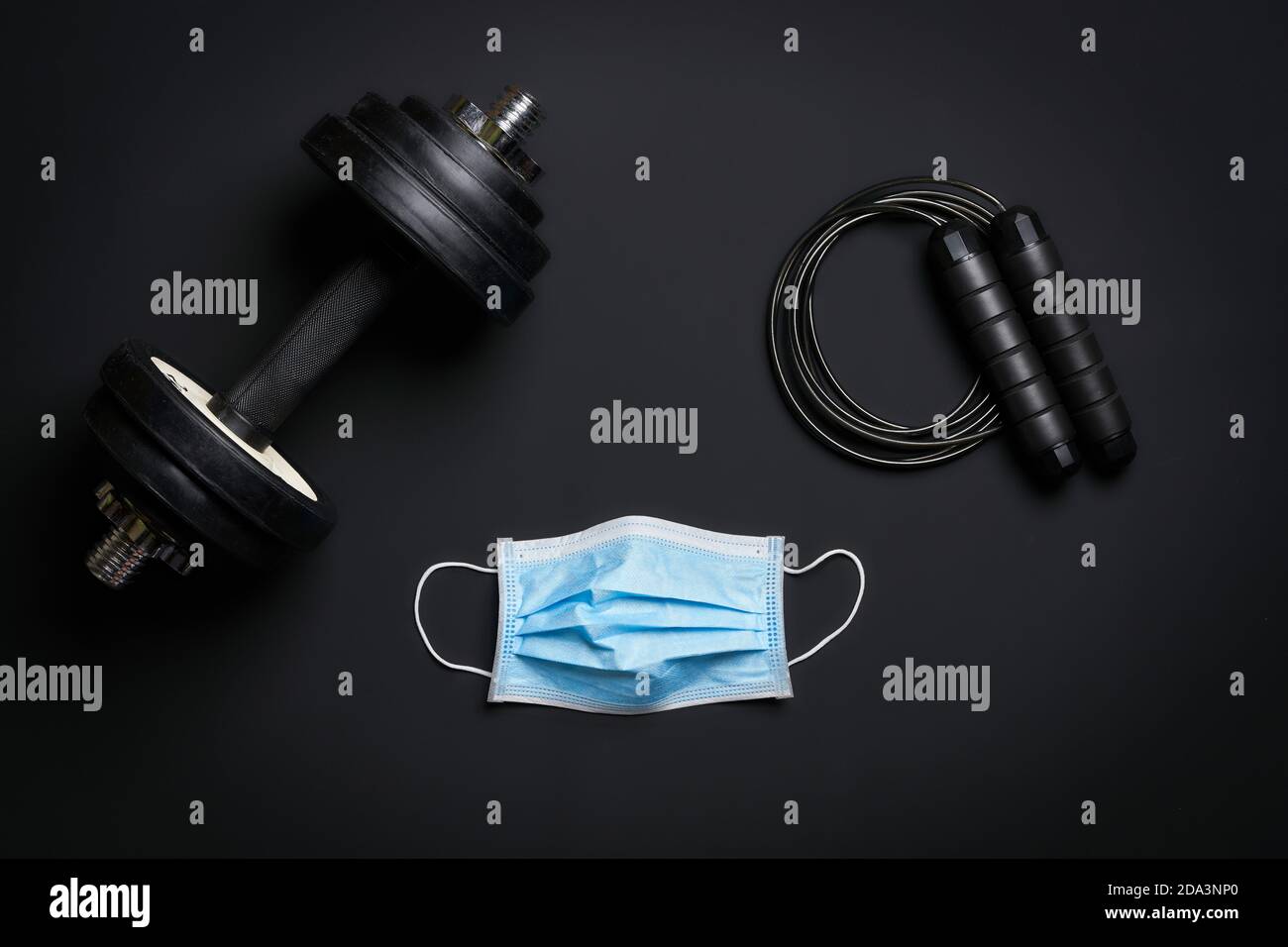 fitness gear dumbbell, jumping rope and protective mask on dark surface