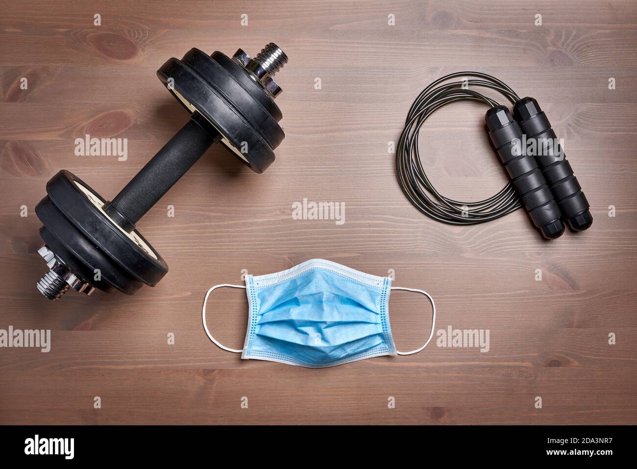 fitness gear dumbbell, jumping rope and protective mask on wooden