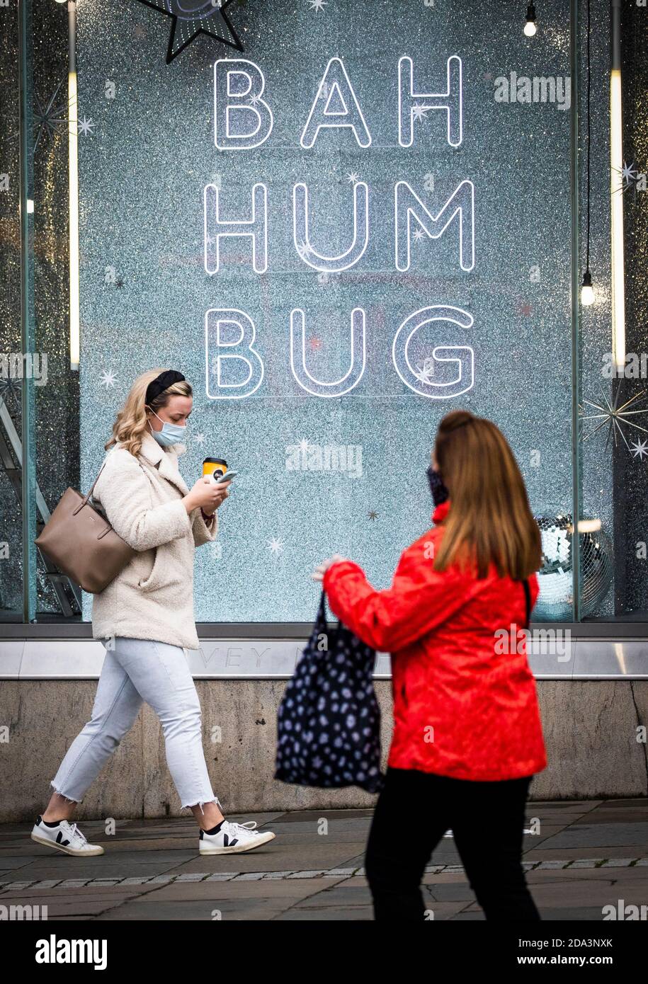 A shopper wearing a protective face mask walks past a shop sign that read 'Bah Humbug' in Edinburgh city centre. Scotland is currently using a tier system to try and drive down coronavirus cases. Stock Photo
