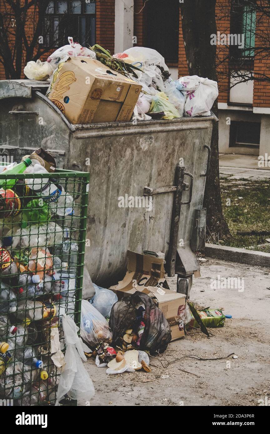 Trash dumpster being overfull with garbage in the city, vertical image. Concept of environmental and ecology problem, land pollution and plastic waste. Stock Photo