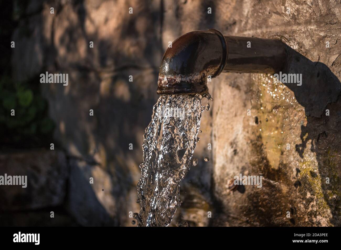Old iron tap water pipe on the road, close up. Water flows constantly. Stock Photo
