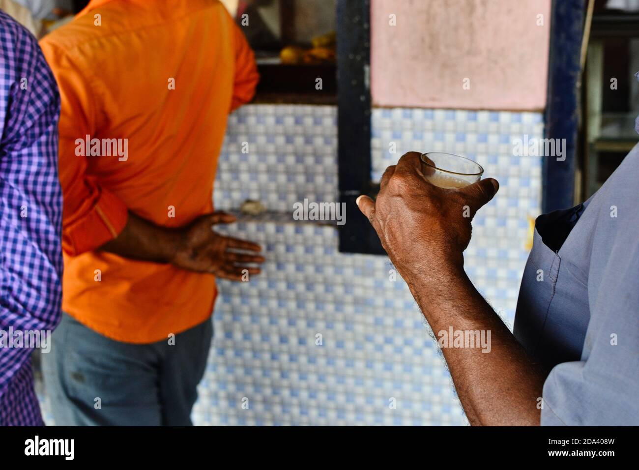 Man holding glass of Indian tea with milk and spices also called masala tea or chai. Men waiting in line near cafe on the railway station in Varkala Stock Photo