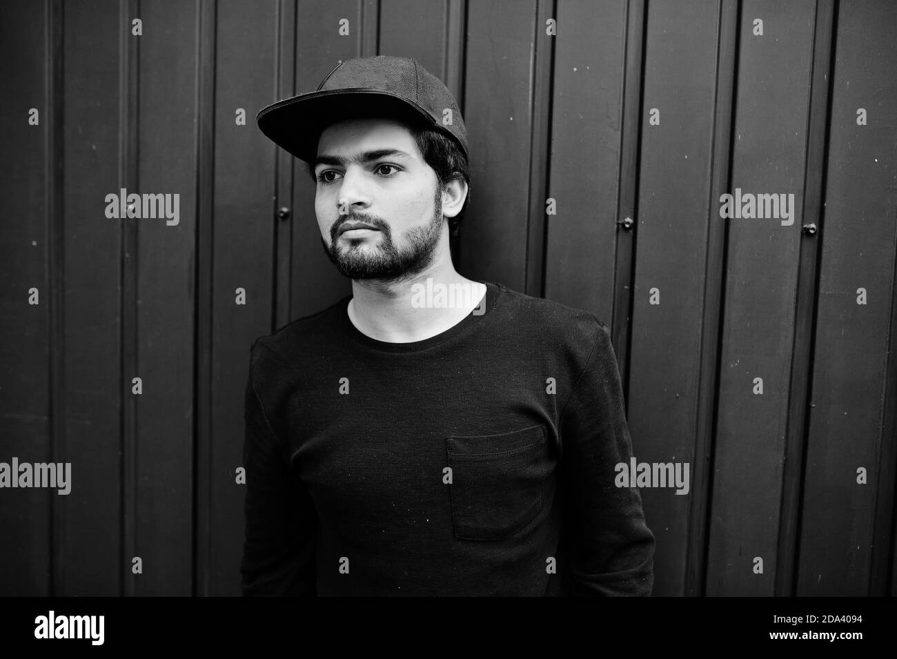 Urban young hipster indian man wear all in black. Cool south asian guy in full cap. Stock Photo