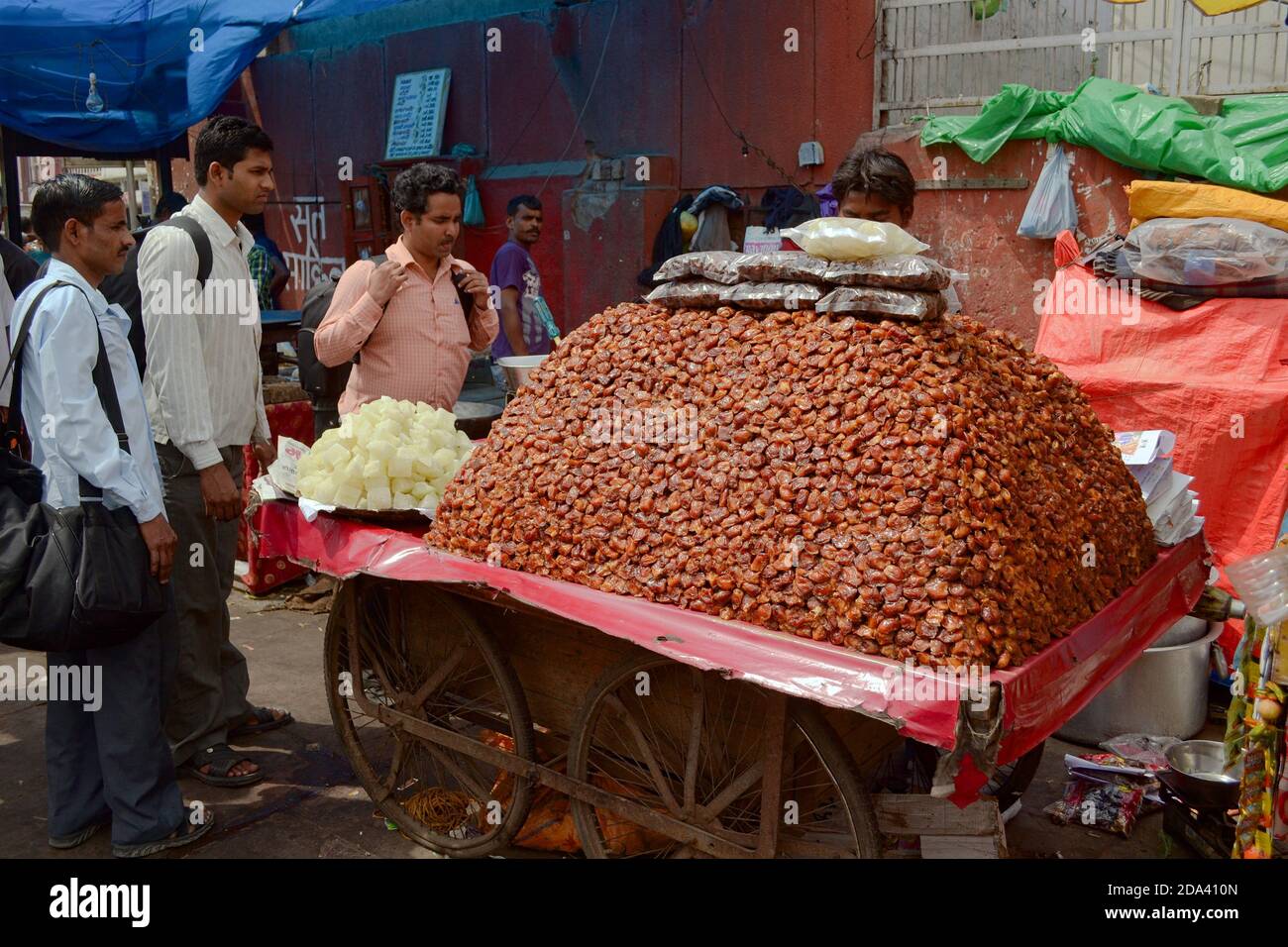 Delhi, India - April, 2014: Big heap of dry dates fruits on a wooden cart on wheels . Man selling sweet foods on the street market stall Stock Photo